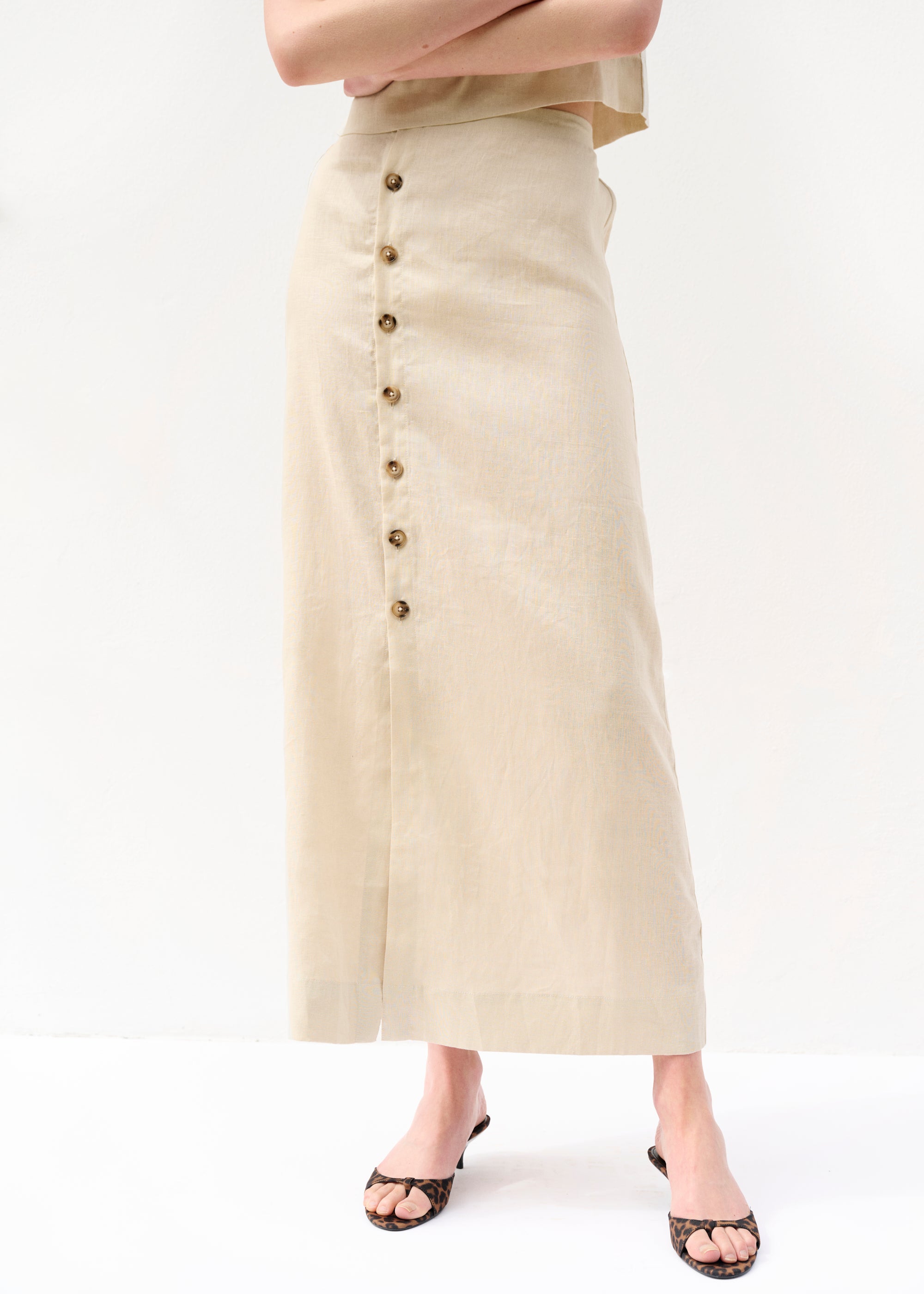 Nahaufnahme des beigefarbenen Rocks aus Leinen mit betonter Knopfleiste. Die Knöpfe sind groß und rund mit einem natürlichen Glanz.