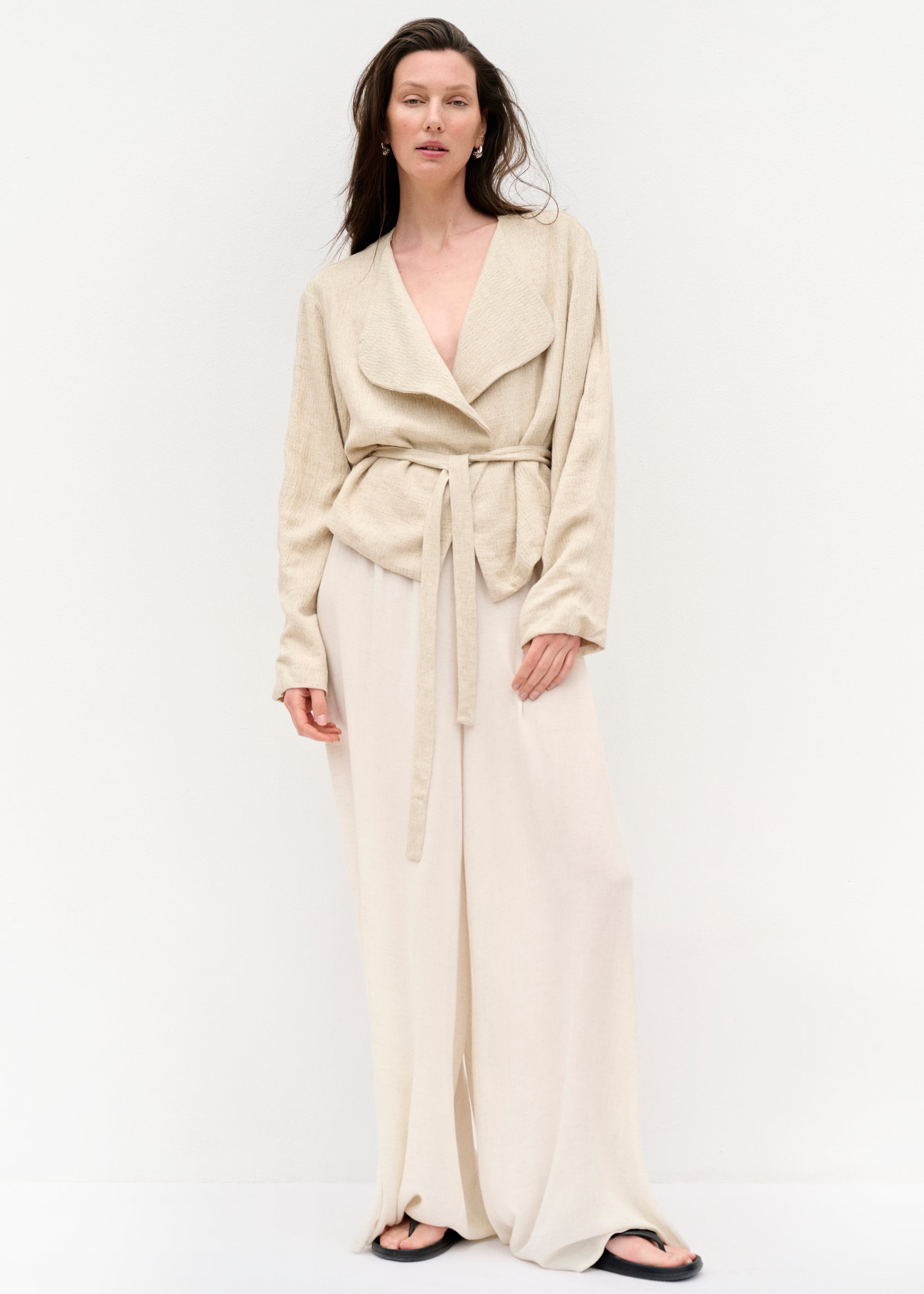 Frontansicht mit geschlossener Jacke, der Gürtel ist gebunden und betont die Taille; darunter trägt das Model keine sichtbare Bluse.