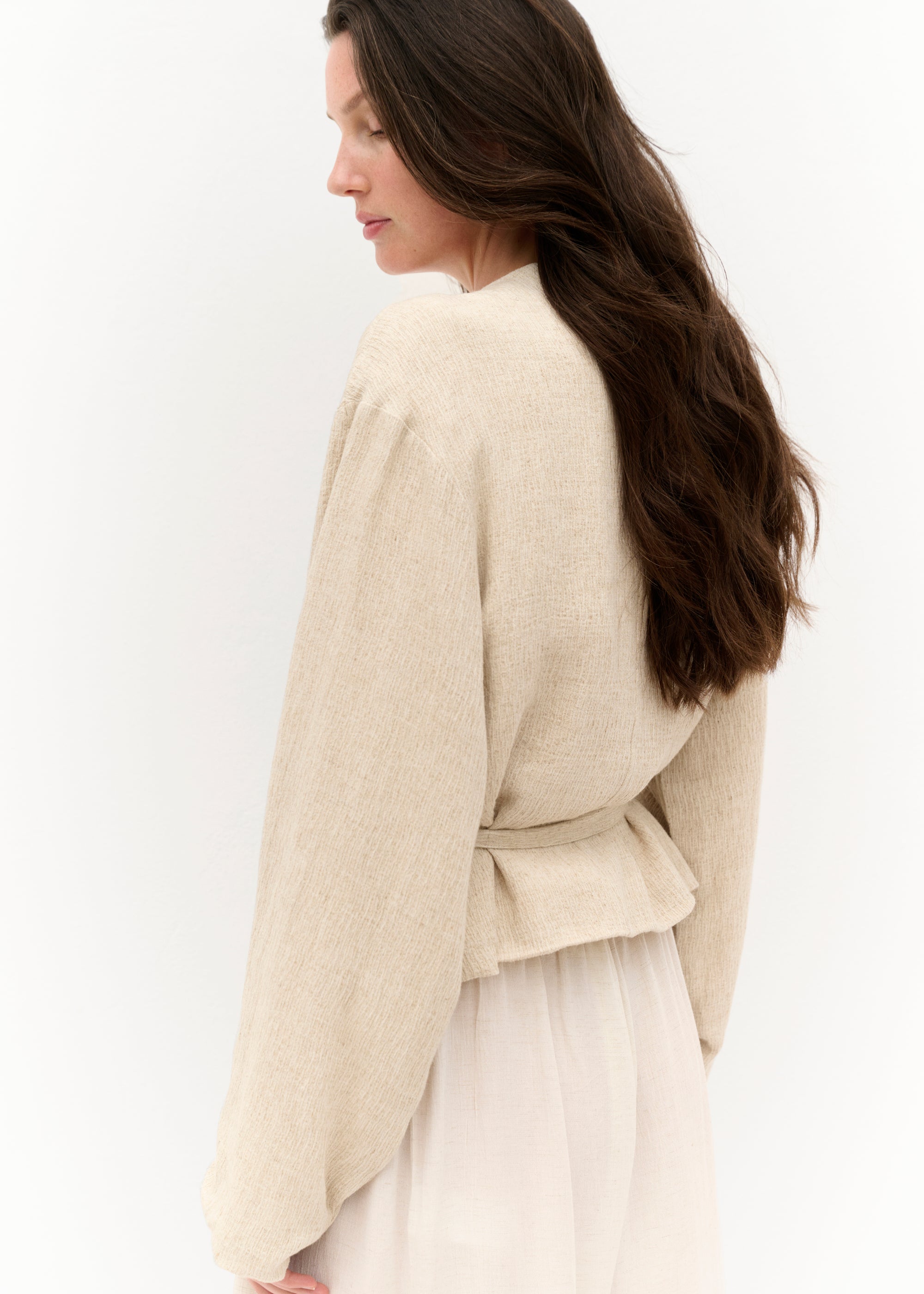 Seitliche Nahaufnahme der Wickeljacke mit Fokus auf die Struktur des Stoffes und den schlichten Schnitt.