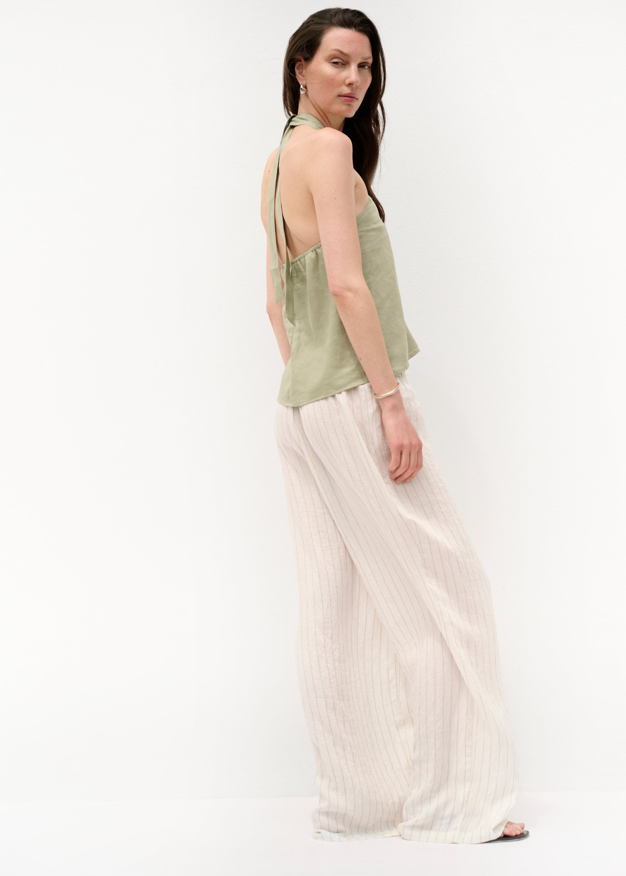 Seitenansicht: Das Top ist am Nacken gebunden und zeigt den freien Rücken. Die Hose fällt weich über ihre Beine.