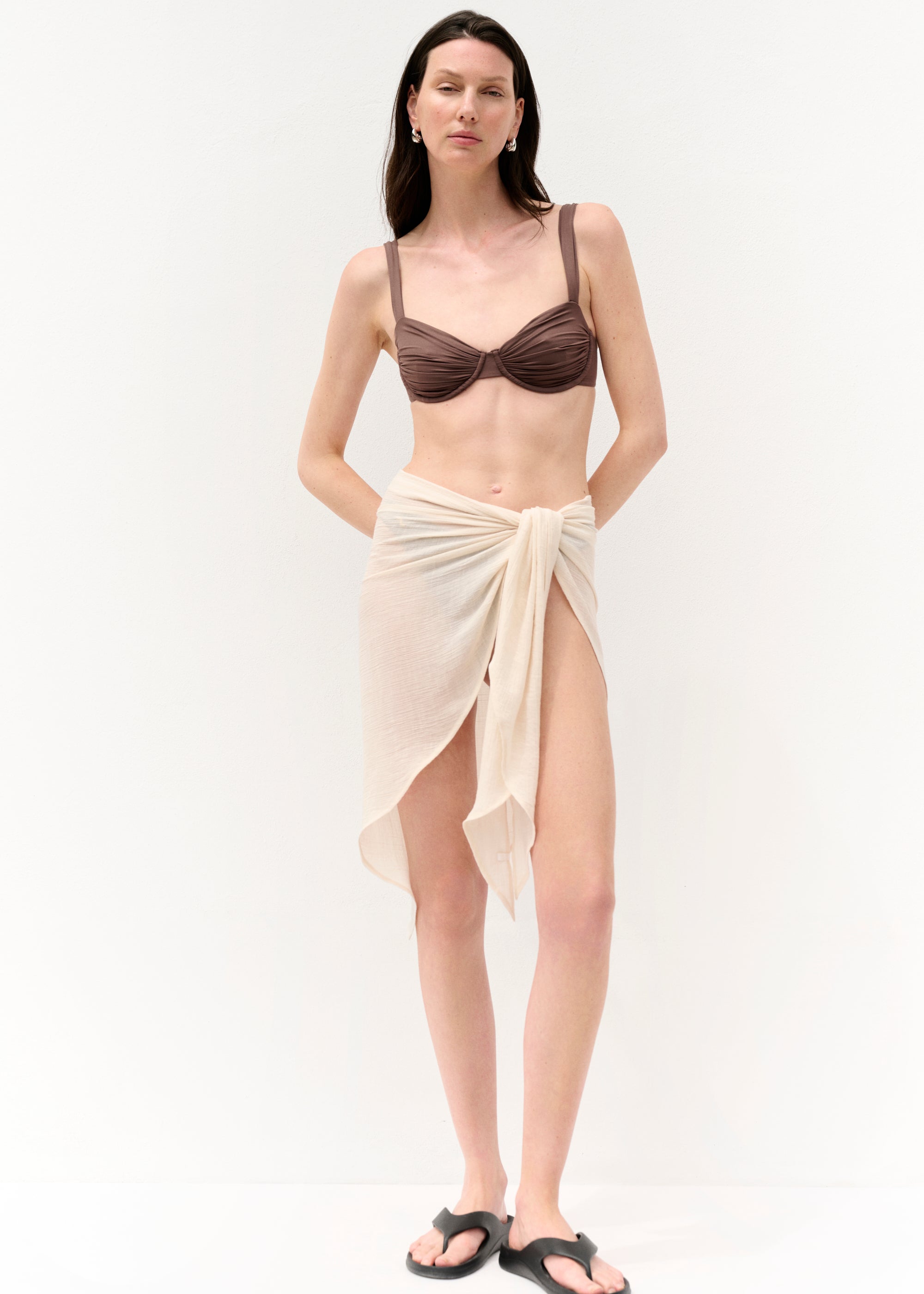 Alttext (für alle drei Bilder, da aus gleichem Shooting & Outfit):
Eine Frau mit langen braunen Haaren trägt ein zartes, transparentes Ensemble aus einer hellen, weit geschnittenen Hose und einem langen, fließenden Kimono mit Gürtel. Darunter trägt sie ein braunes Bikinioberteil. Die Aufnahmen zeigen sie stehend und gehend vor weißem Hintergrund, mit natürlichem Licht und leicht wehenden Stoffen.