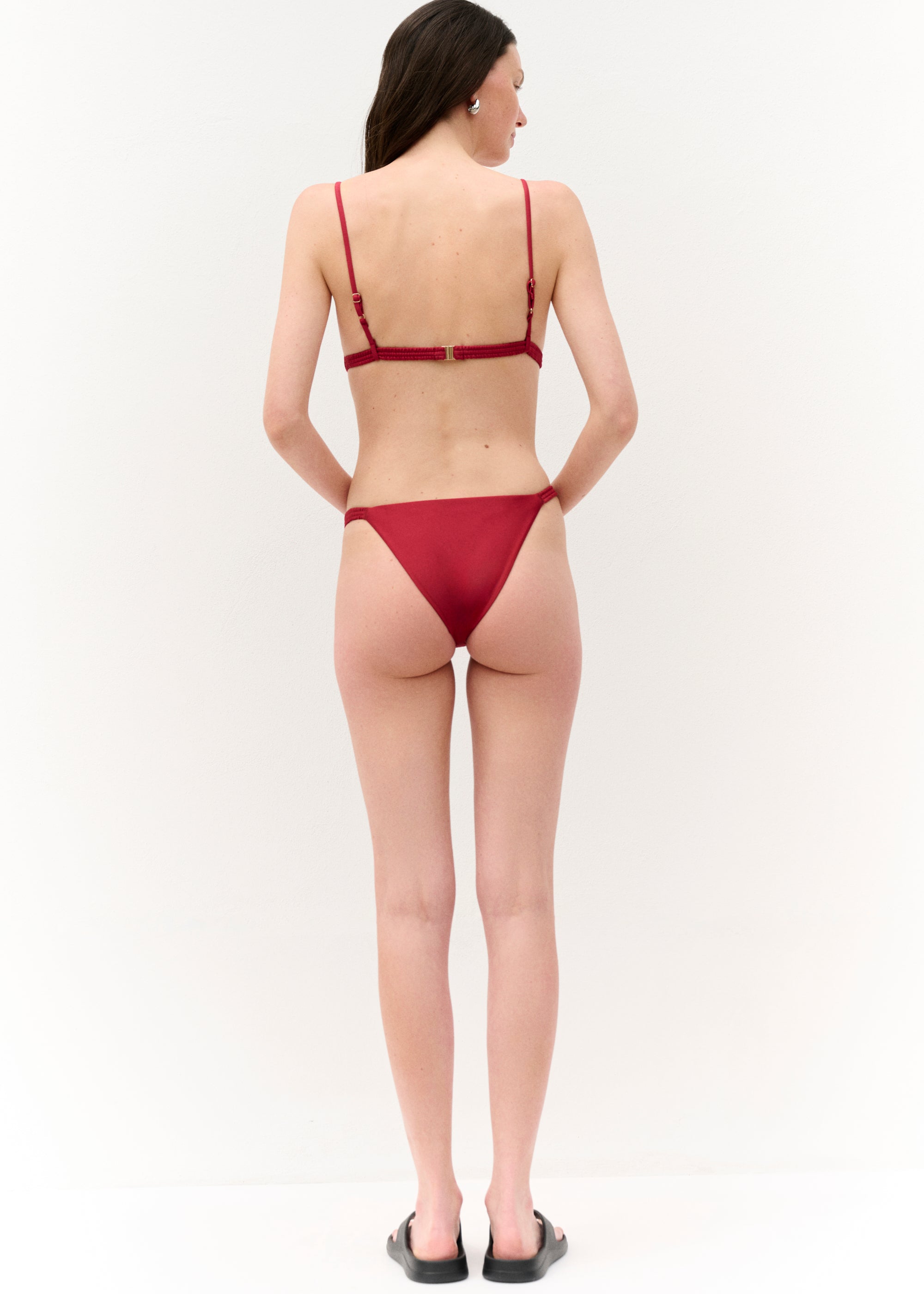 Rückansicht
Die Frau ist von hinten zu sehen. Das Bikini-Oberteil wird mit einem goldenen Verschluss geschlossen, die schmalen Träger sind verstellbar. Das Höschen ist knapp geschnitten und zeigt eine hohe Beinausschnitthöhe.