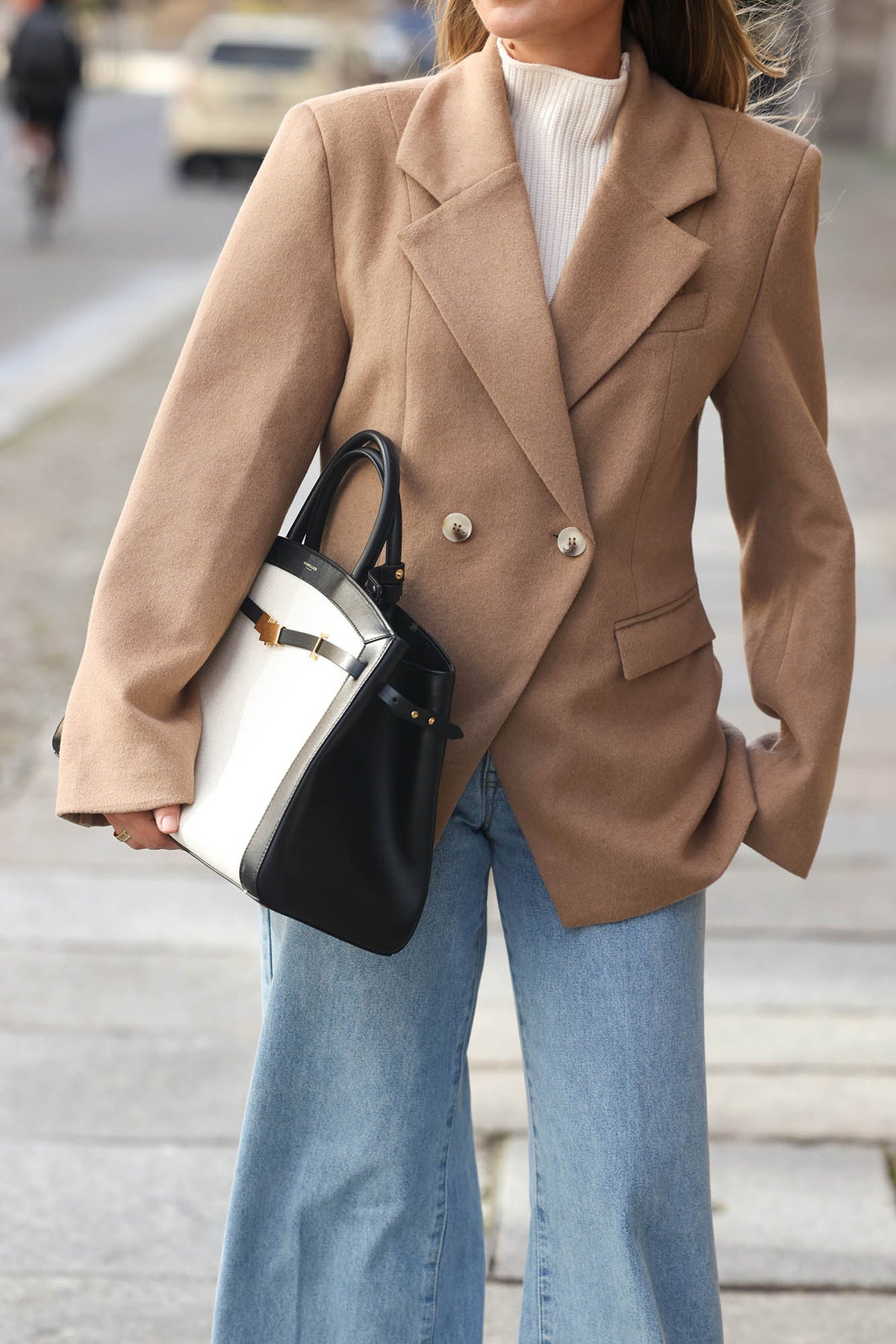 Detailaufnahme des beigefarbenen Doppelreiher-Blazers mit breitem Revers, hellen Knöpfen und Pattentaschen, kombiniert mit weißem Strick und hellblauer Jeans.