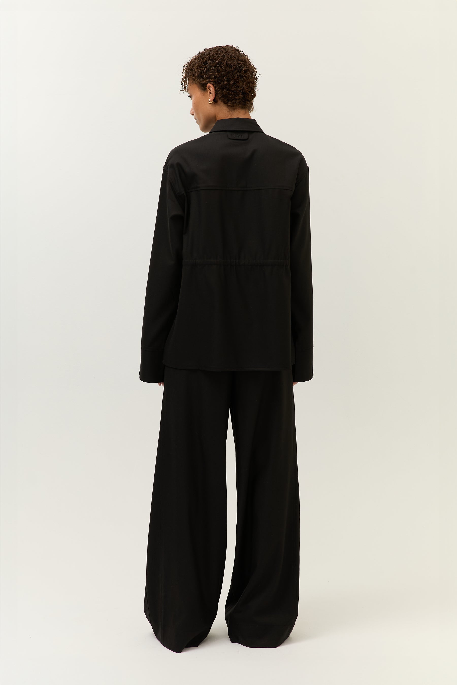 Rückansicht, gebunden
Model von hinten im schwarzen Set mit geraffter Taille und weitem Hosenbein.