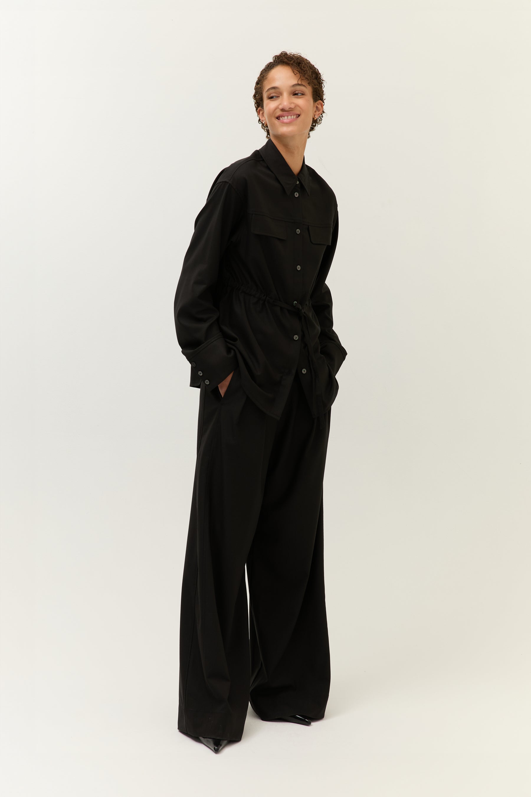 Frontalansicht, gebunden
Schwarzer Utility-Zweiteiler mit Taillierung durch Kordelzug, Hemdjacke mit Kragen, weite Hose.