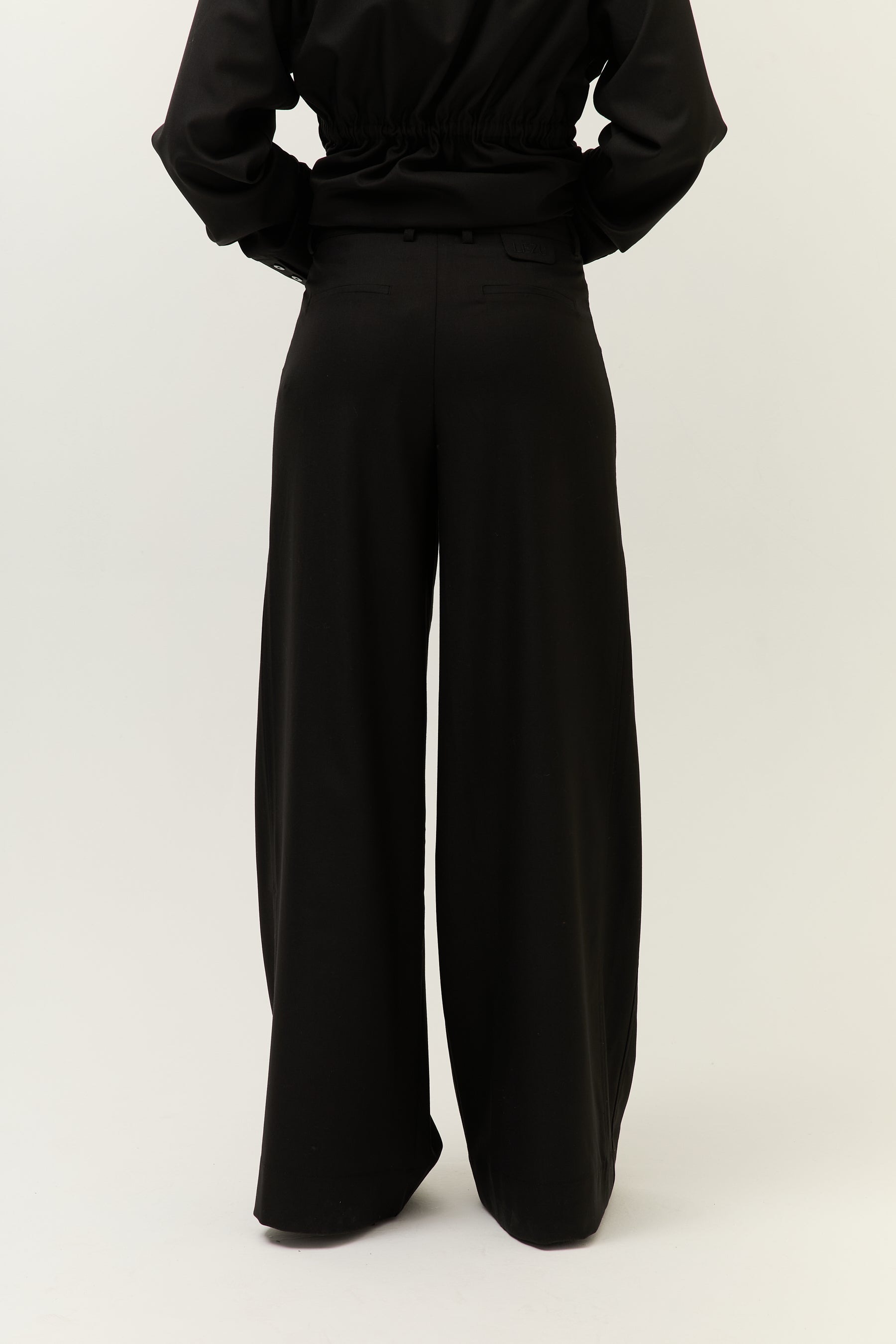Rückansicht Hose
Rückseite der weiten schwarzen Hose mit schmalen Gesäßtaschen und Gummizug im Saumbereich des Hemds.