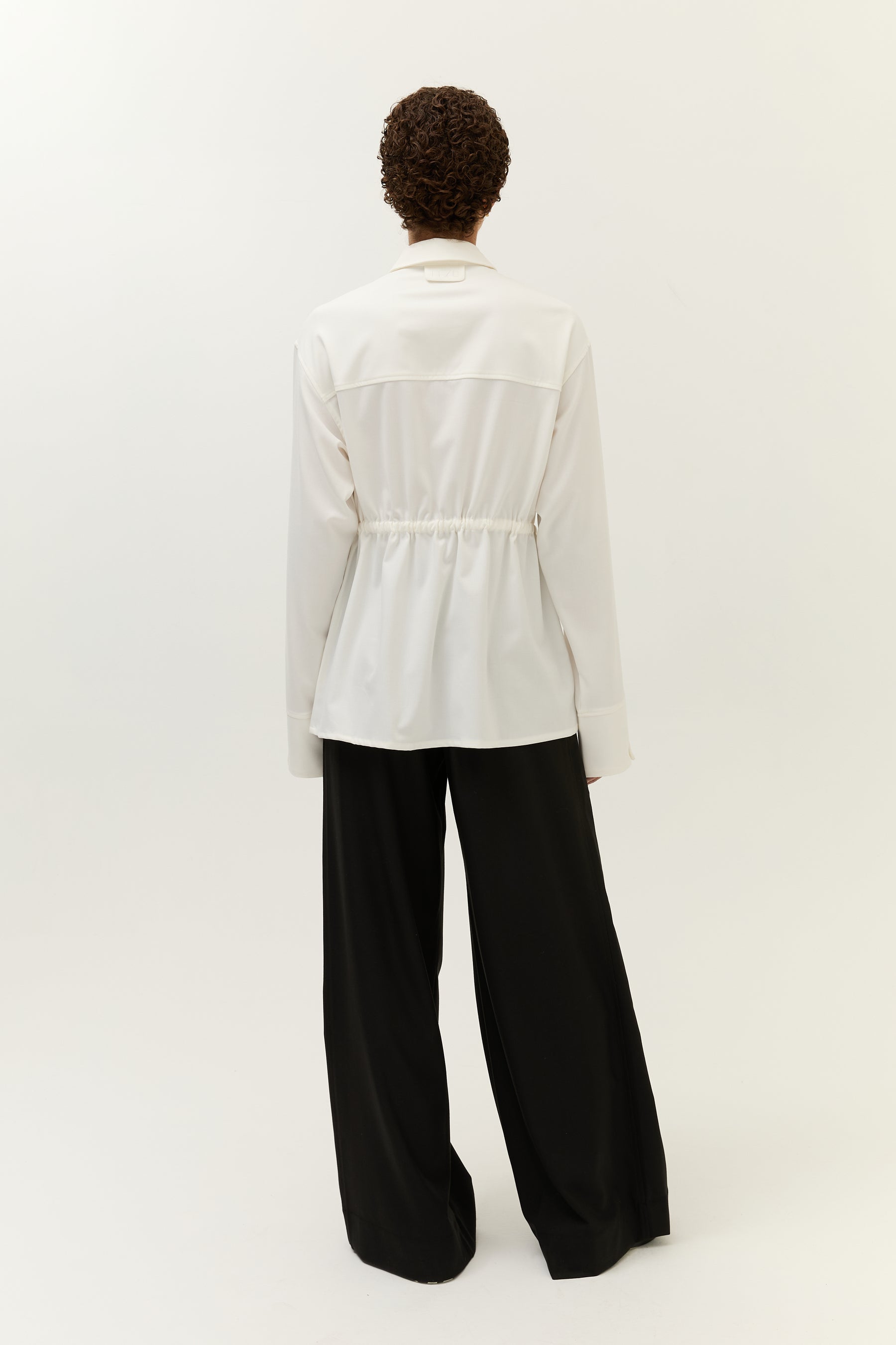 Rückansicht des Outfits mit betonter Taille durch den Tunnelzug, schwarze weite Hose sichtbar.