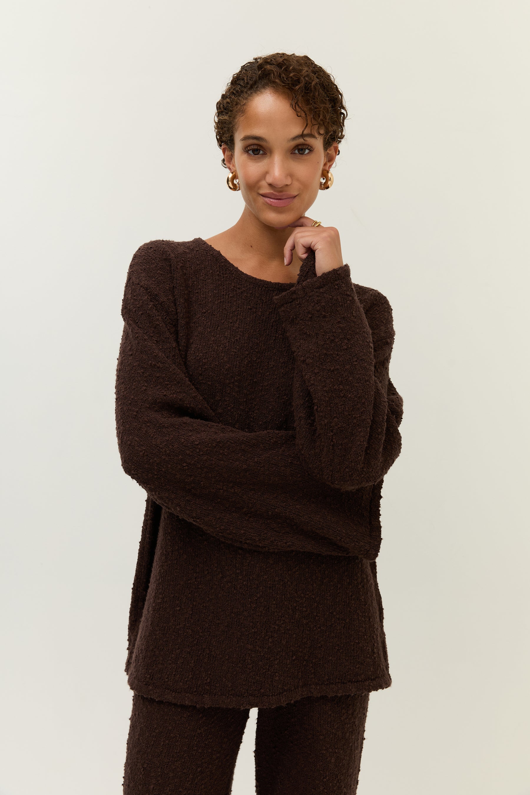 Das Model zieht leicht am Oberteil, wodurch der lockere Sitz und der weiche Fall des Bouclé-Stoffs sichtbar wird.