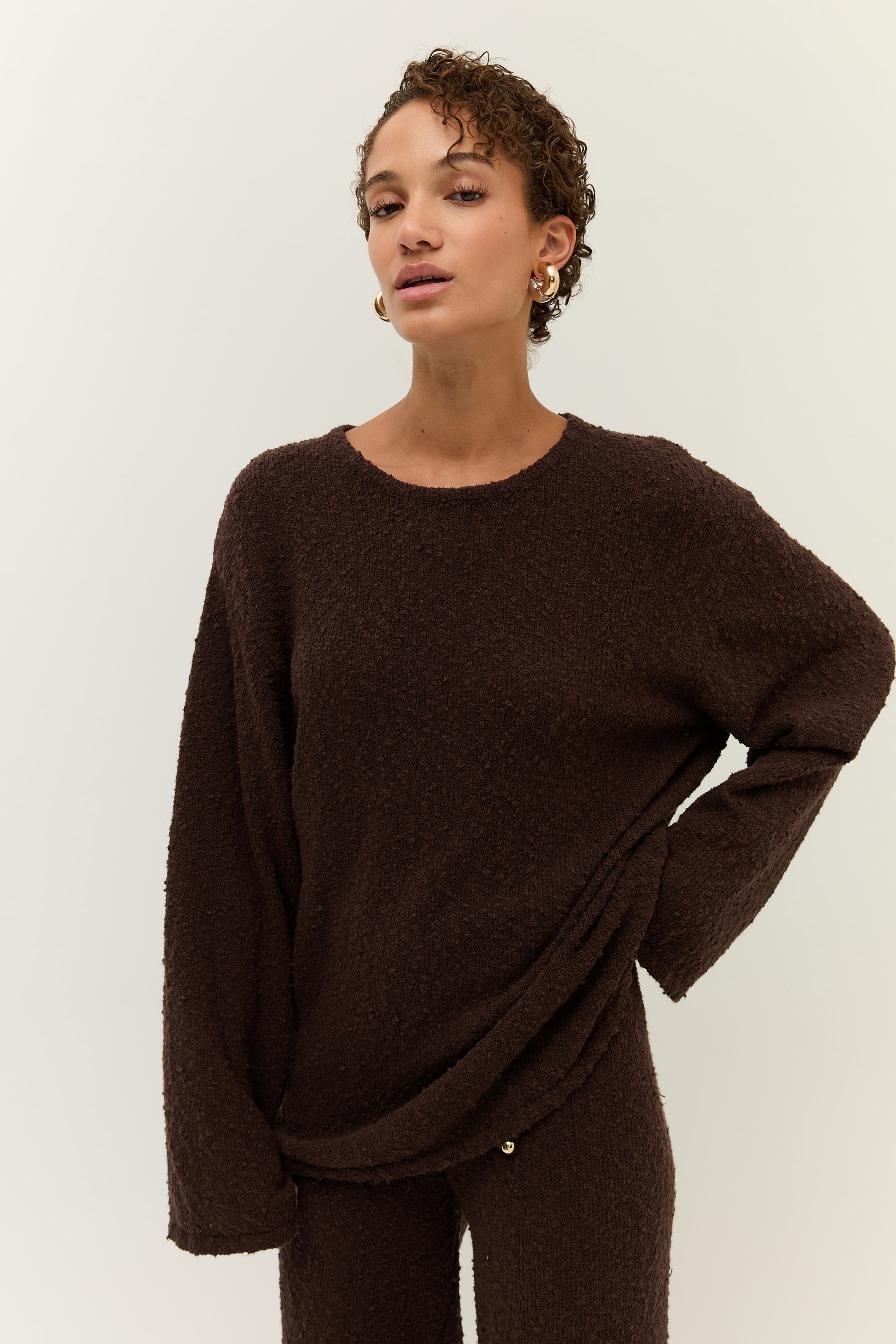 Model trägt ein entspannt geschnittenes Ensemble aus braunem Bouclé-Strick mit weitem Oberteil und ausgestellter Hose.