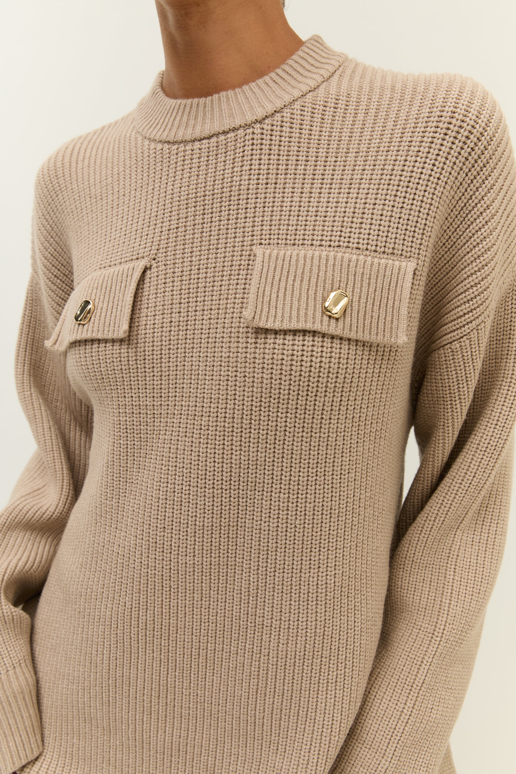 Detailansicht Brustbereich
Nahaufnahme der goldfarbenen Knopfdetails auf den beiden Brusttaschen eines grob gestrickten Kleides.