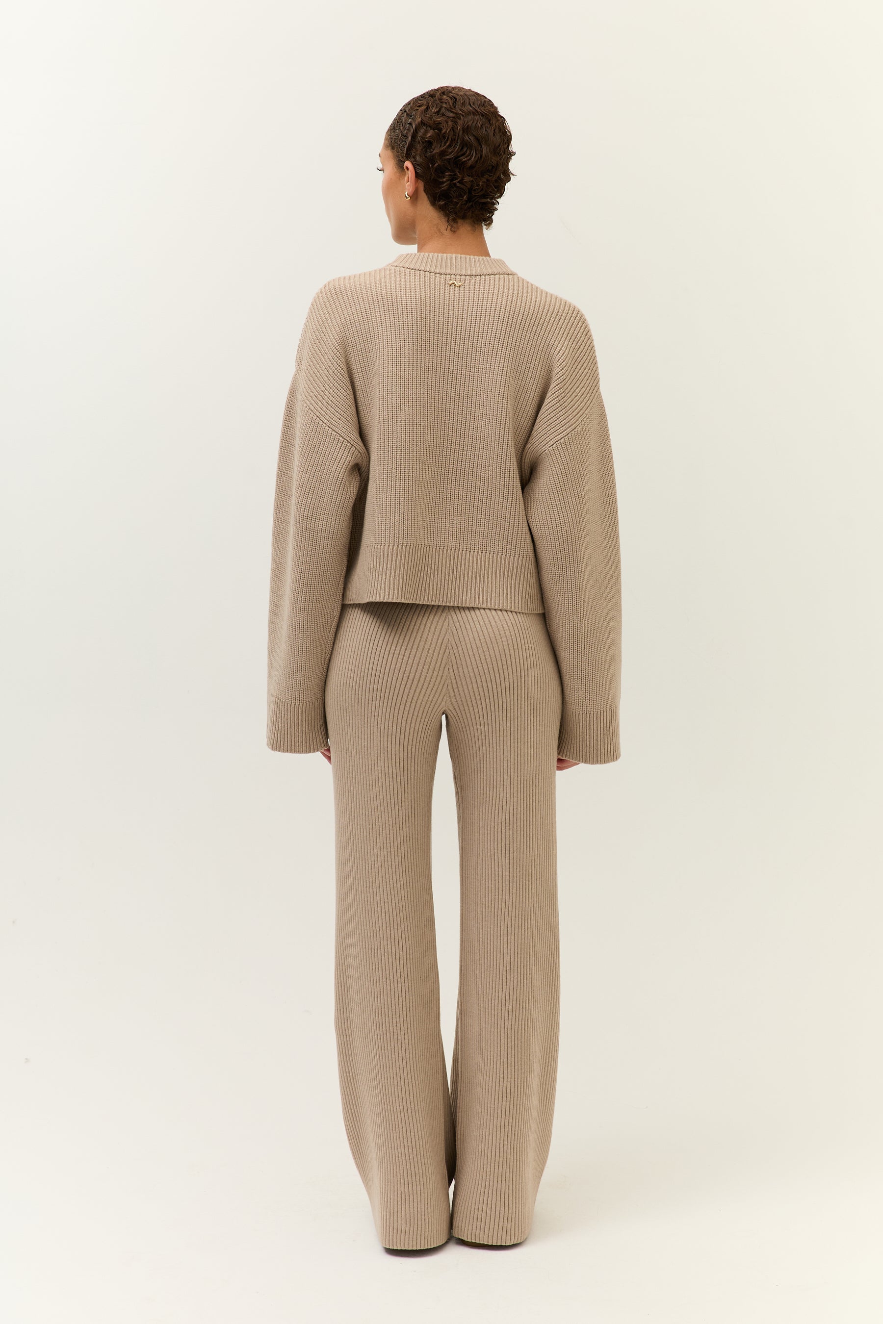 Rückansicht des Outfits – locker fallender Pullover und gerade geschnittene Hose mit weitem Bein.