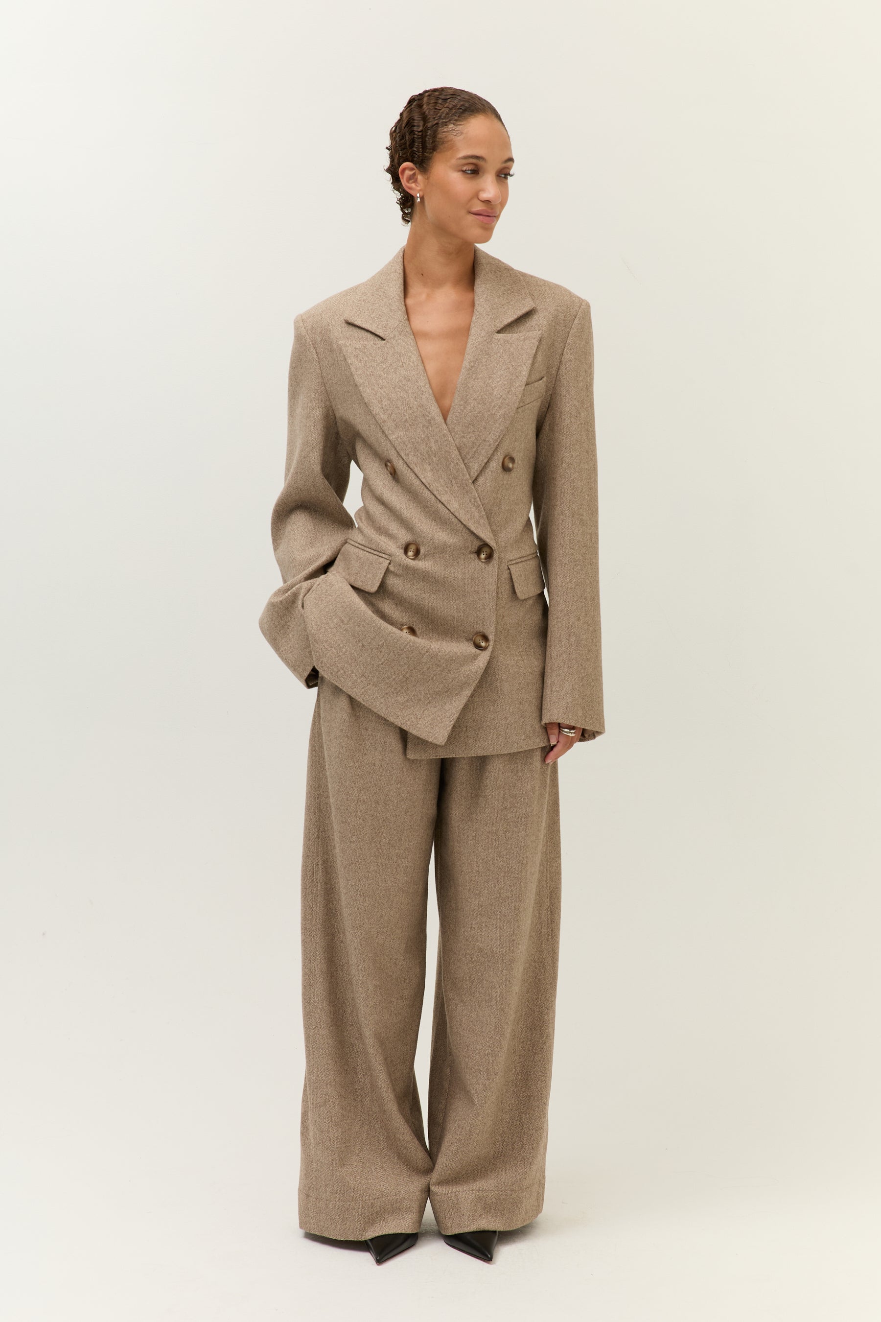 Ganzkörperaufnahme des Models in einem beigefarbenen Hosenanzug mit doppelreihigem Blazer und weiten Anzughosen.
