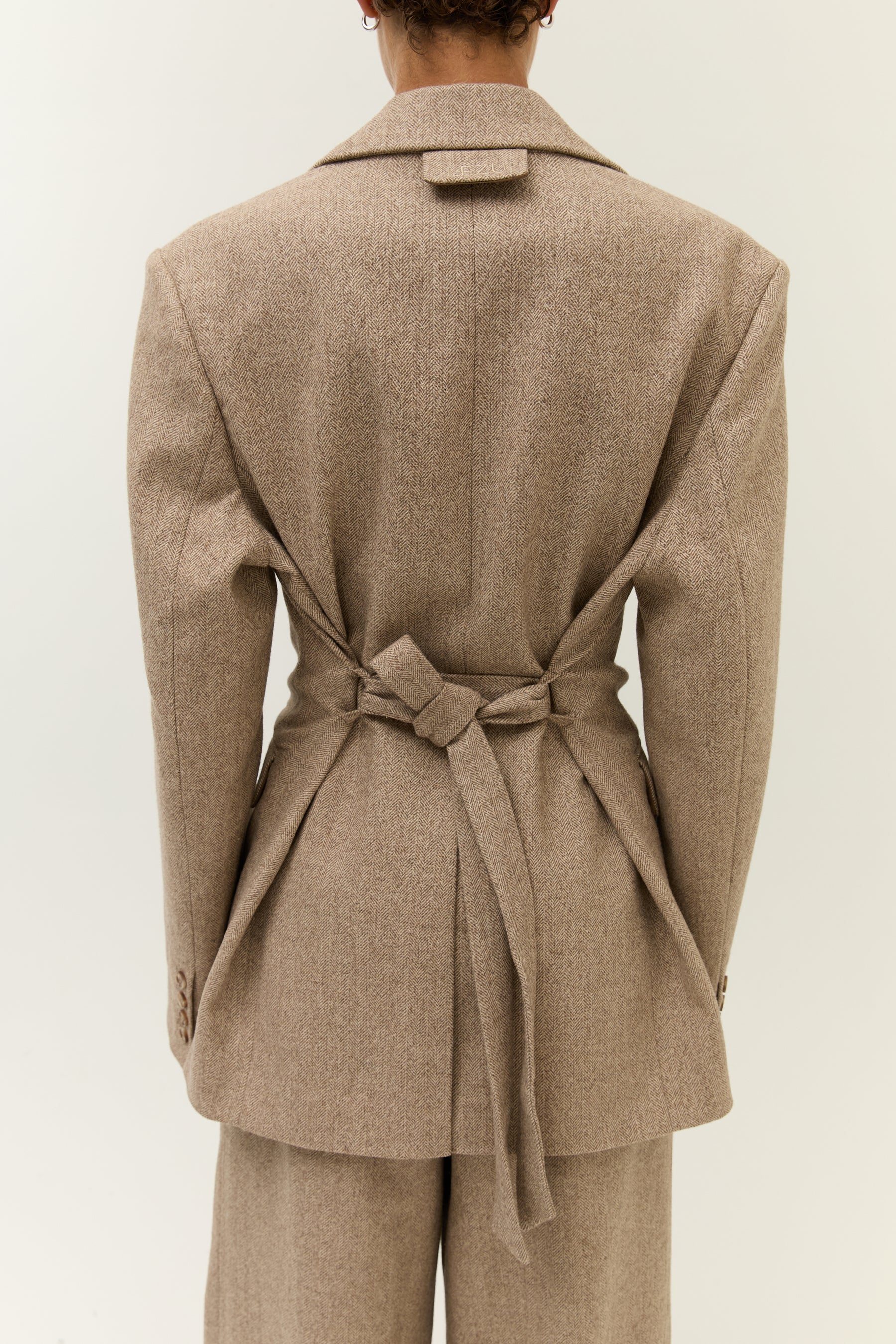 Rückenansicht des Blazers mit Gürtel, der hinten zu einer Schleife gebunden ist und die Taille betont.