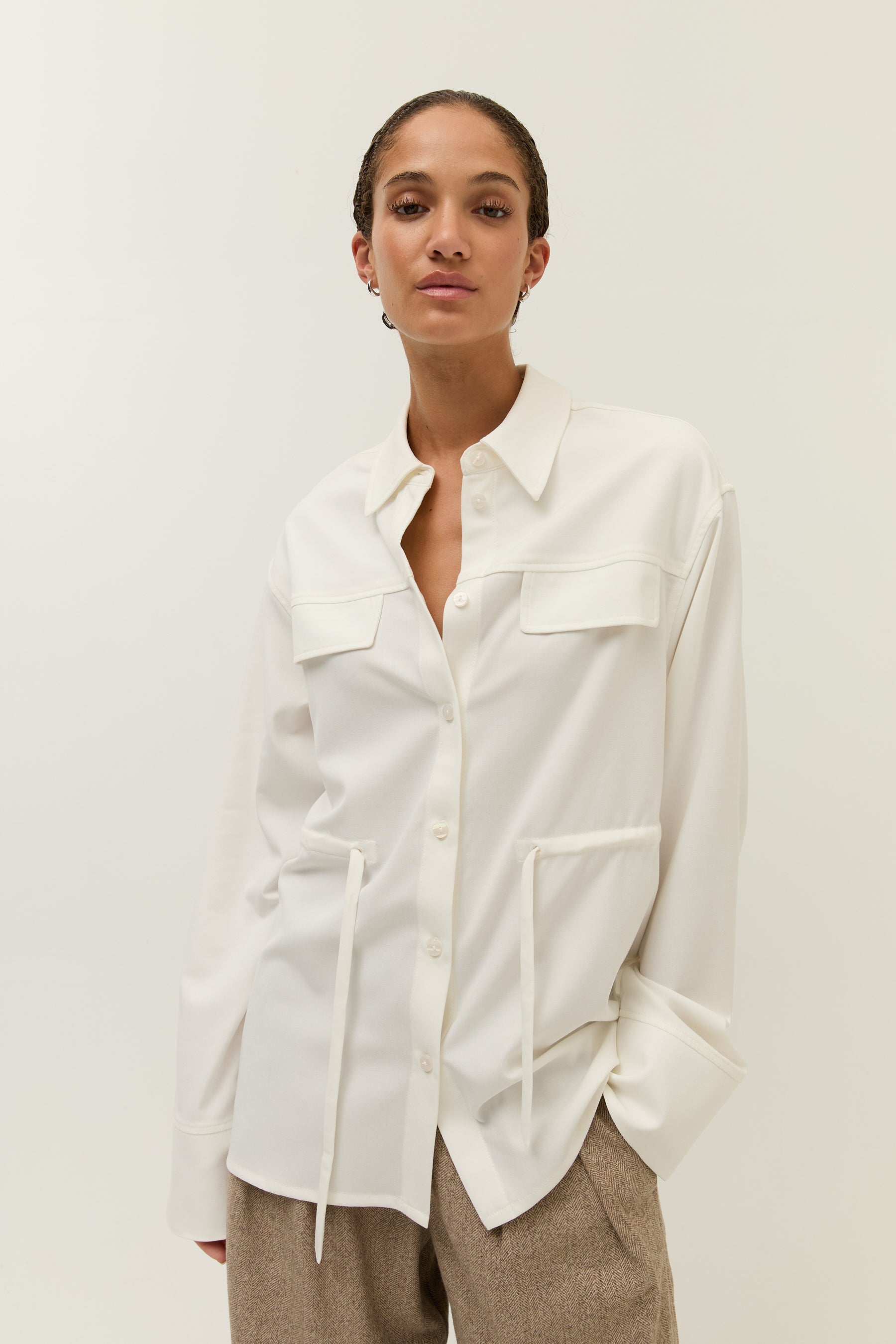 Frau trägt das gleiche Hemdblusenshirt locker über einer braunen weiten Hose, ohne Taillierung gebunden.