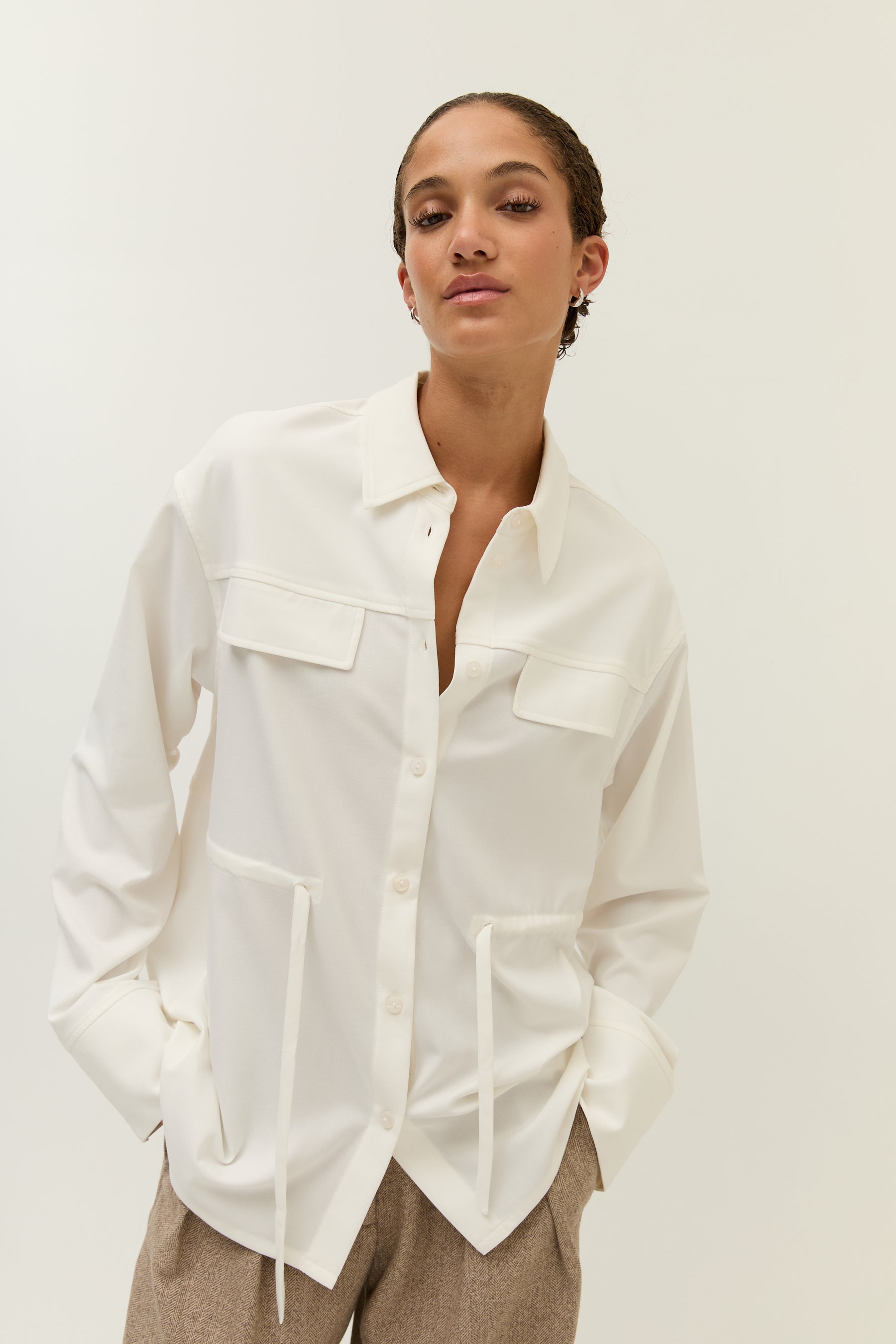 Die gleiche Pose aus einem leicht anderen Winkel, Fokus auf das geöffnete Oberteil und die Seitentaschen.