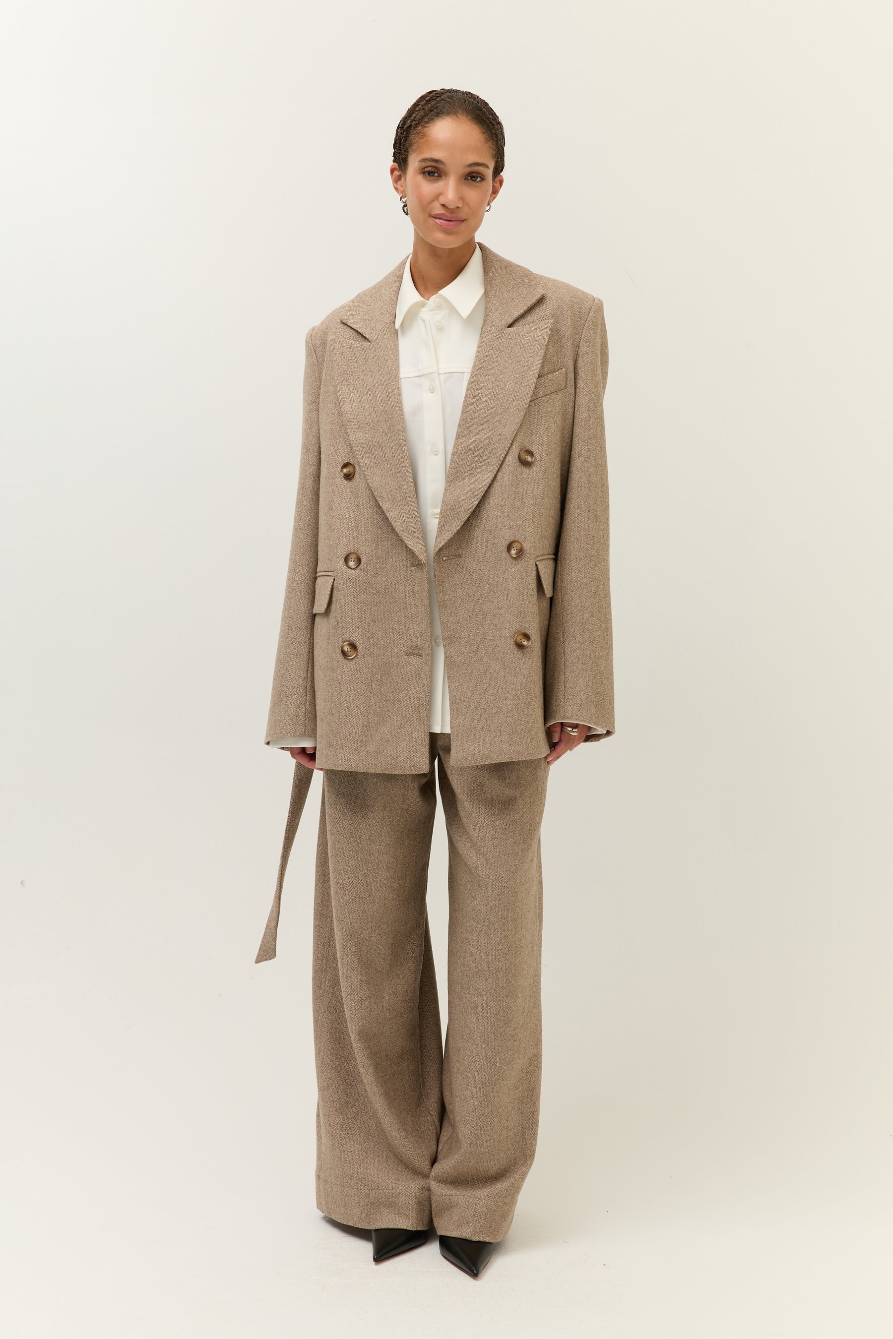 Frontale Ganzkörperaufnahme des Models mit weißem Hemd unter dem offenen Blazer und passender weiter Hose.