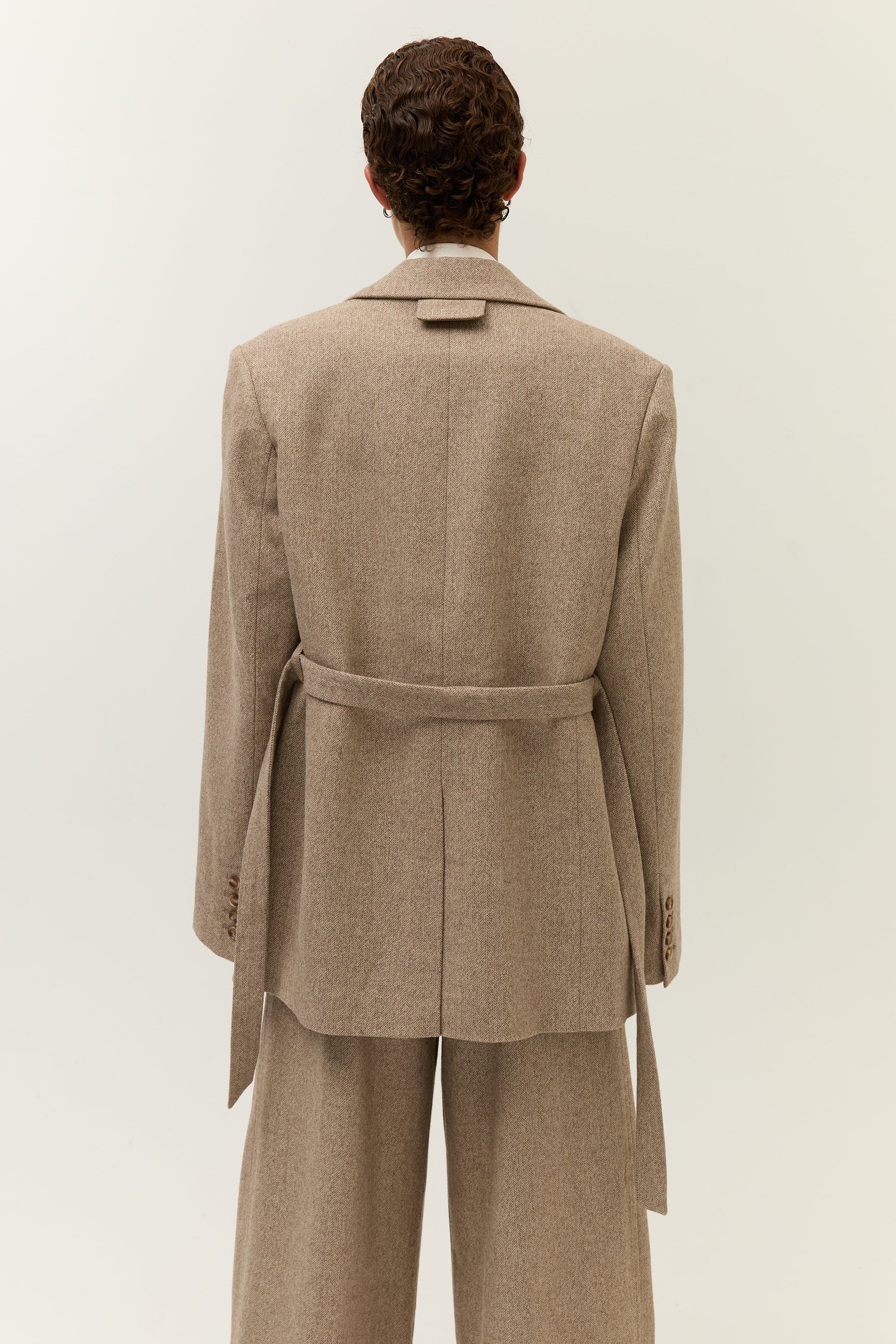 Rückenansicht des geöffnet getragenen Blazers, bei dem der Gürtel locker durch die Gürtelschlaufen geführt ist.