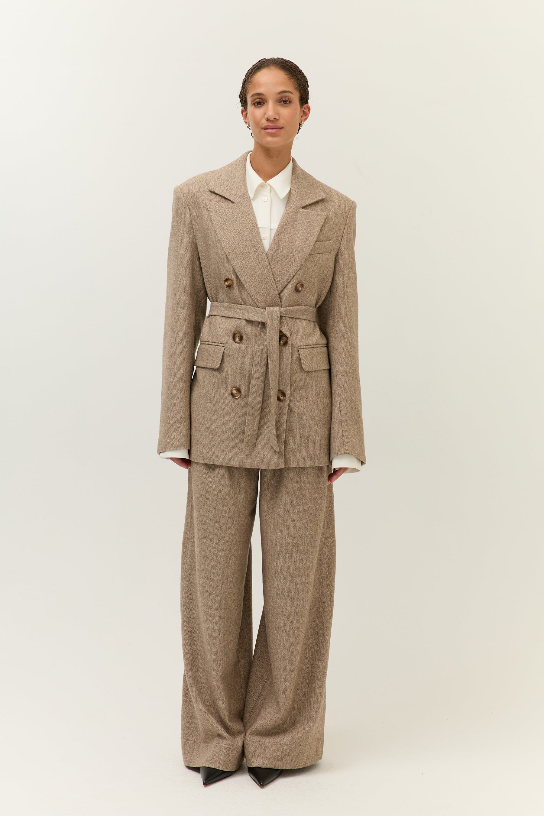 Frontansicht mit geschlossenem Gürtel-Blazer (leichte Variation)
Model frontal im taillierten Zweiteiler mit Gürtelblazer und weiter Hose aus Wollmix.