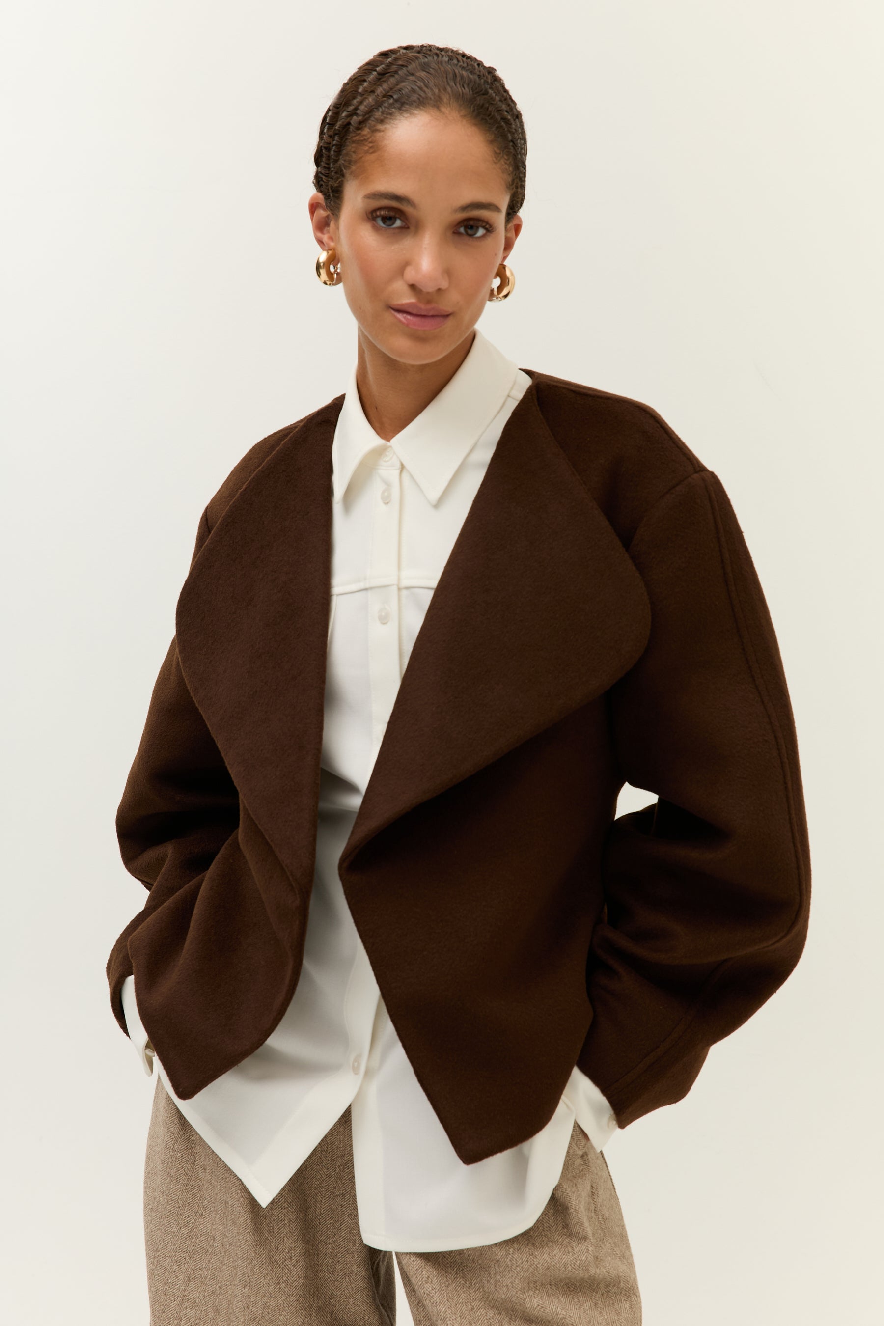 Halbnahe Frontansicht, Hände in den Taschen: Jacke locker offen getragen, darunter die strukturierte weiße Hemdbluse sichtbar.