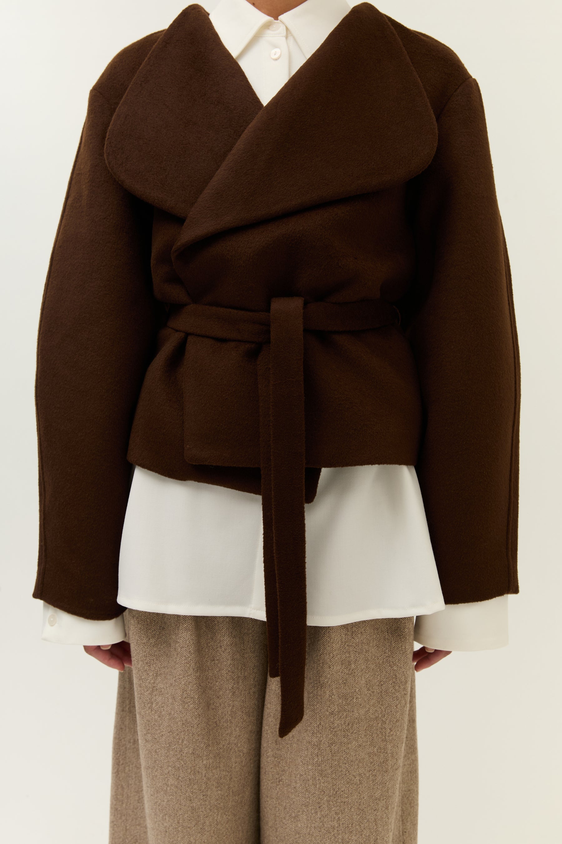 Nahaufnahme Taillenbereich: Fokus auf die gebundene Jacke, die darunter sichtbare Hemdbluse und die Textur der Hose.