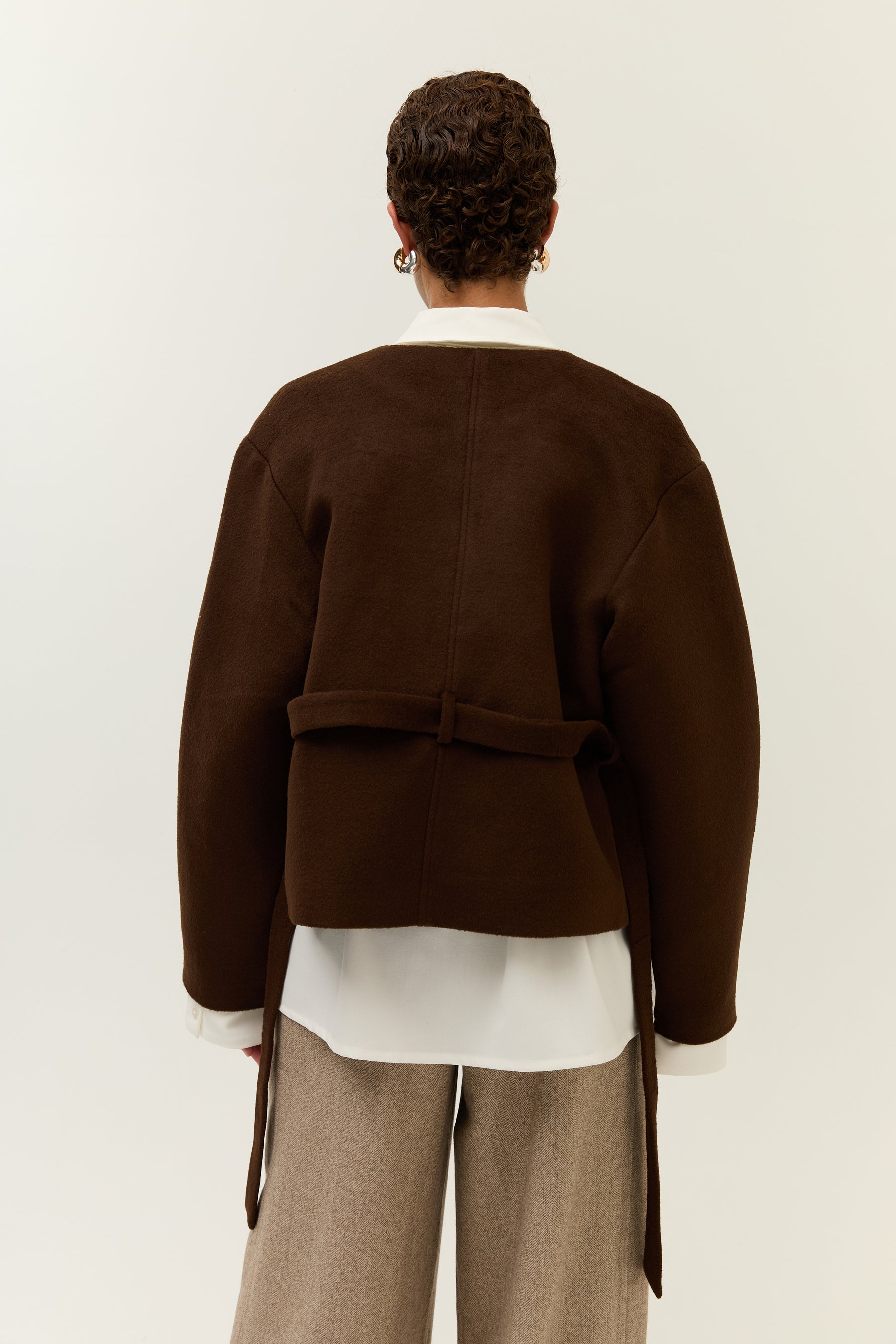 Rückenansicht: Blick auf den Rücken der gebundenen Jacke, die weißen Blusendetails ragen unten hervor.