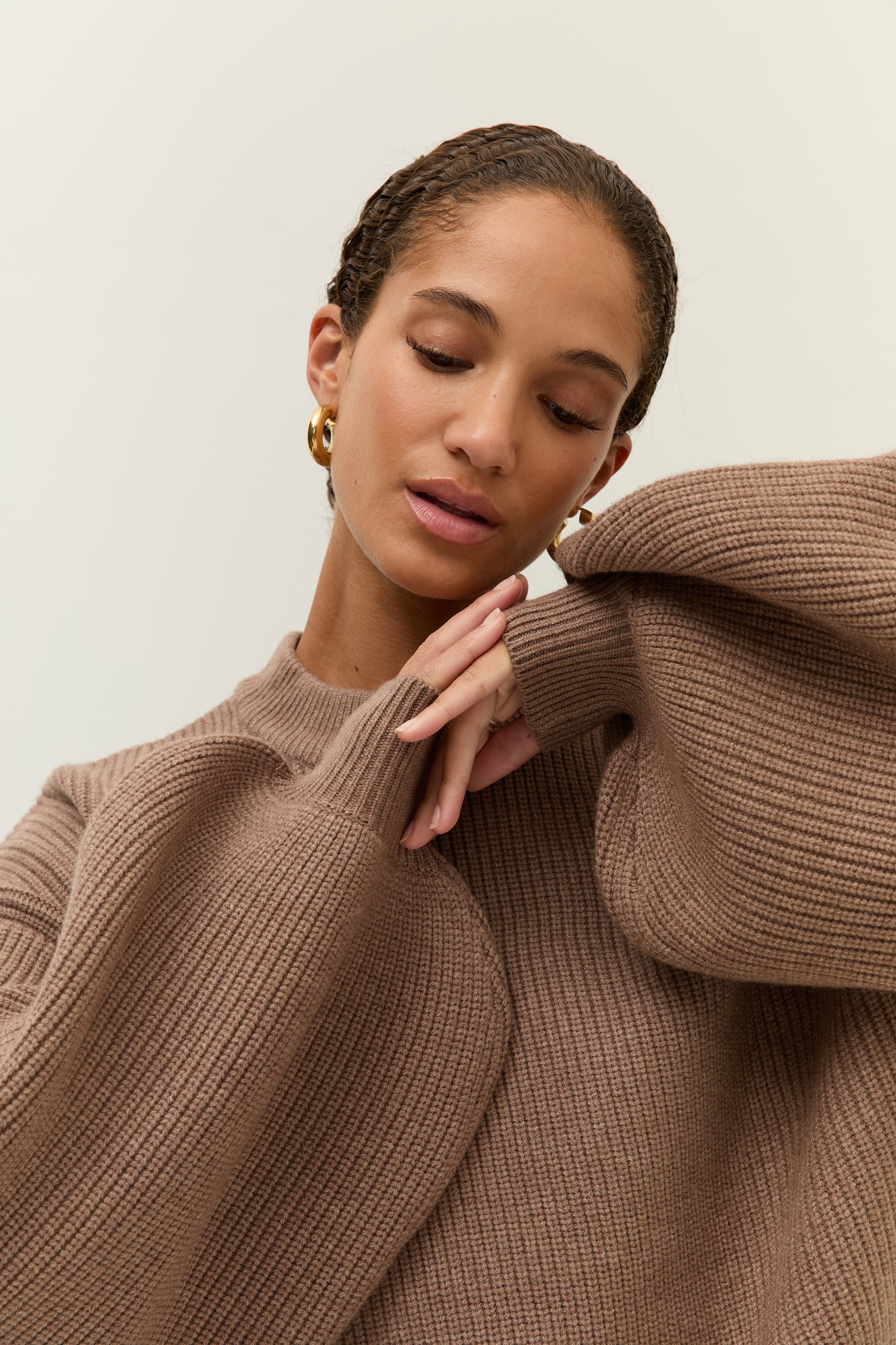 Bild 5: Porträt der Frau mit Blick nach unten, die Arme leicht vor dem Körper verschränkt. Die weiten Ärmel des Pullovers umrahmen das Gesicht.