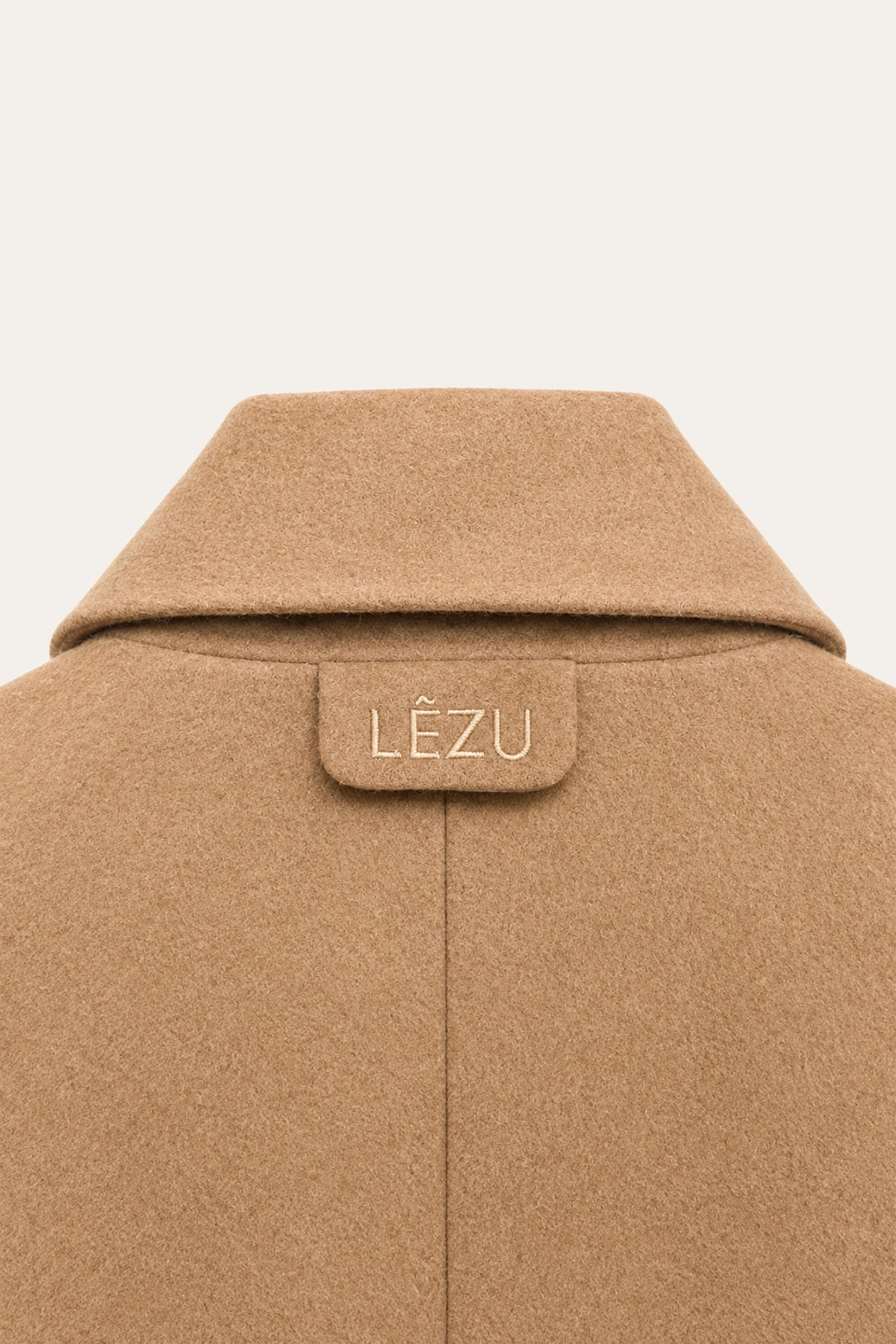 Detailansicht der Rückseite eines camelbraunen Blazers mit breitem Kragen, mittiger Rückennaht und LEZU-Stickerei unterhalb des Kragens.