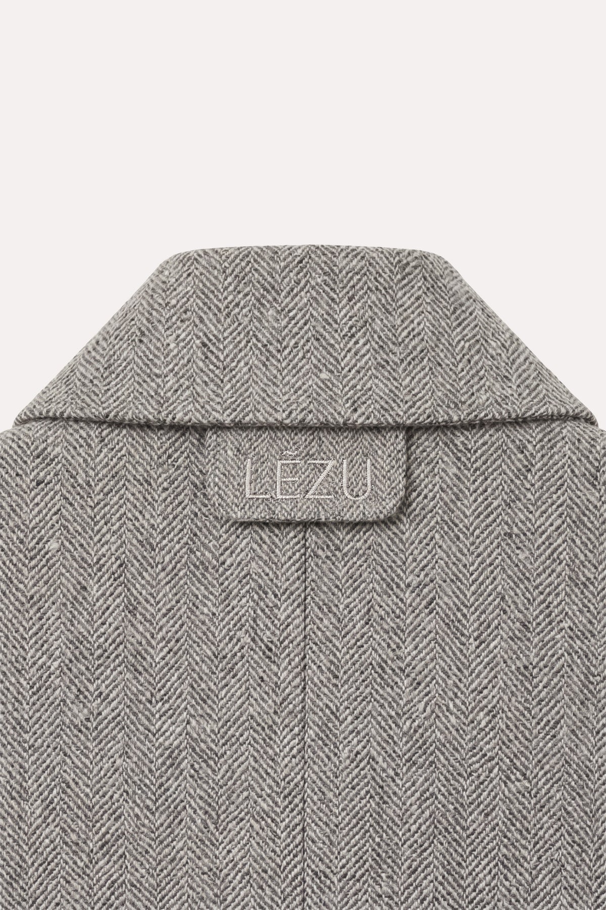 Detailaufnahme des DELIA Blazer Herringbone Grey von hinten: Kragen mit eingeprägtem LEZU-Logo auf einer Lasche und Rückennaht im Fischgrätmuster.