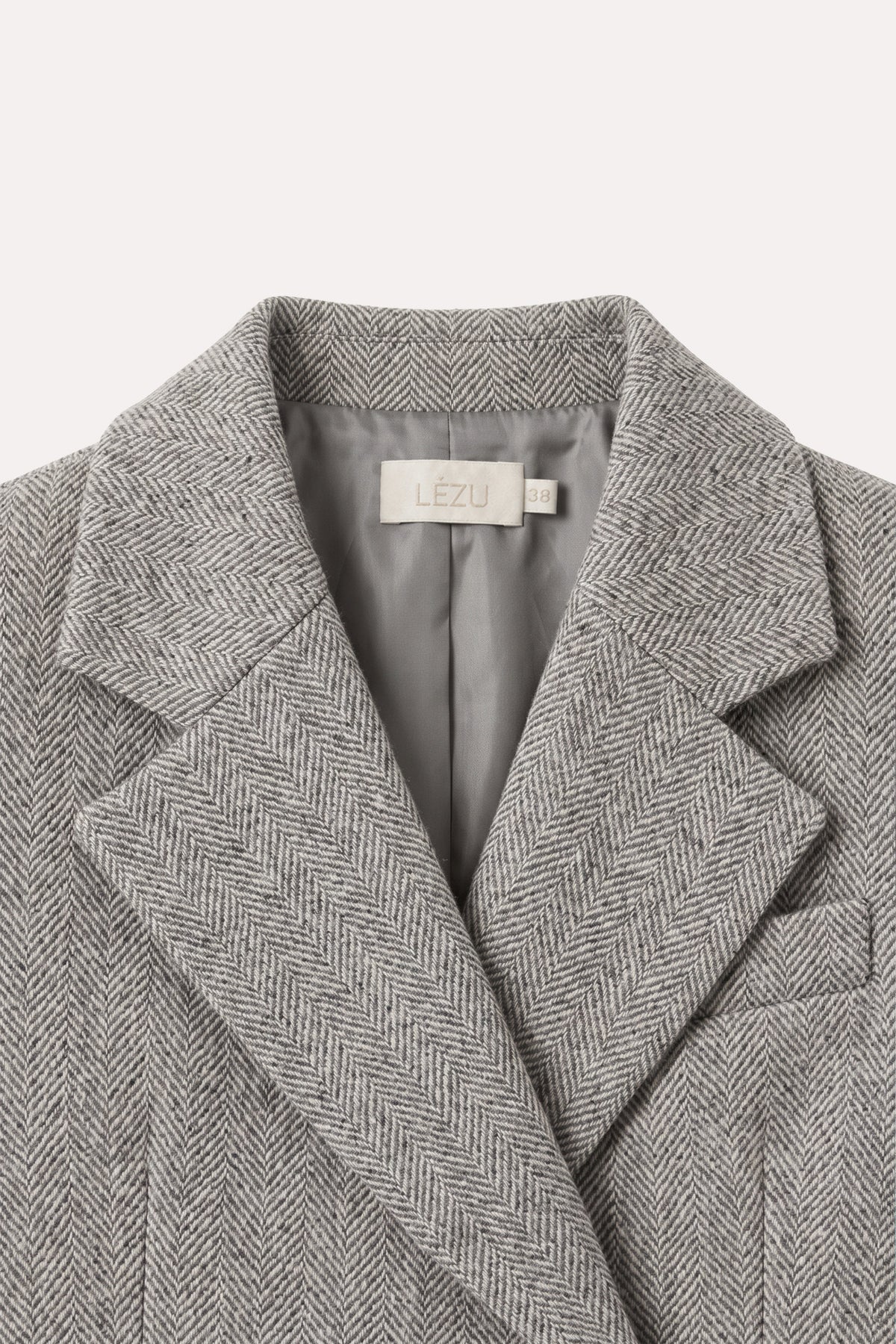 Detailaufnahme des DELIA Blazer Herringbone Grey von vorne: breites Revers, grau gefütterter Innenkragen mit LEZU-Etikett und Brustpattentasche.