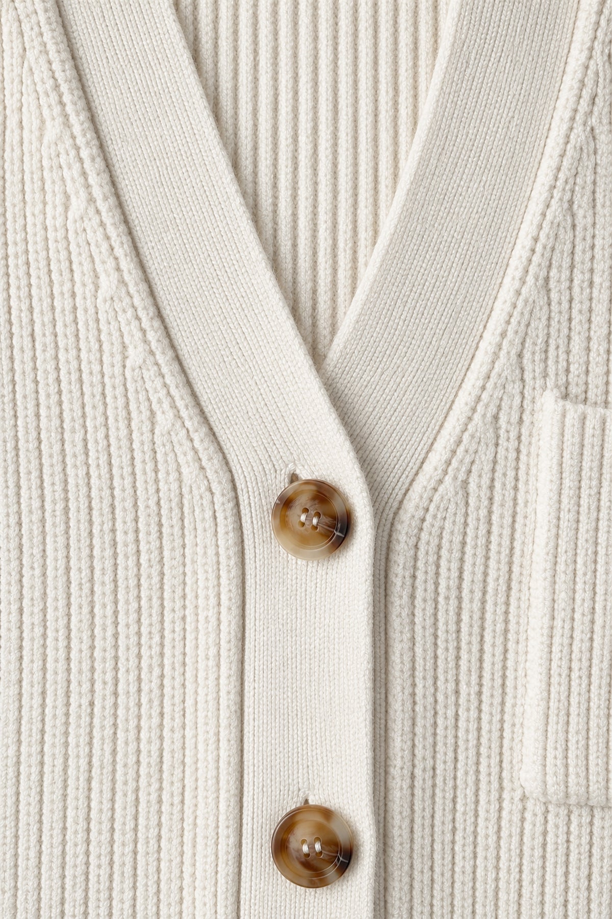 Detailaufnahme einer cremefarbenen Strickjacke mit Rippenstruktur, V-Ausschnitt, braunen Knöpfen und aufgesetzter Tasche.