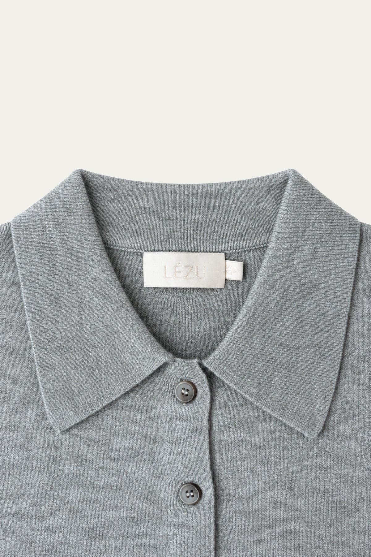 Detailansicht einer hellgrau melierten Strickjacke mit großem Kragen, Knopfleiste und LÉZU-Label im Nackenbereich.