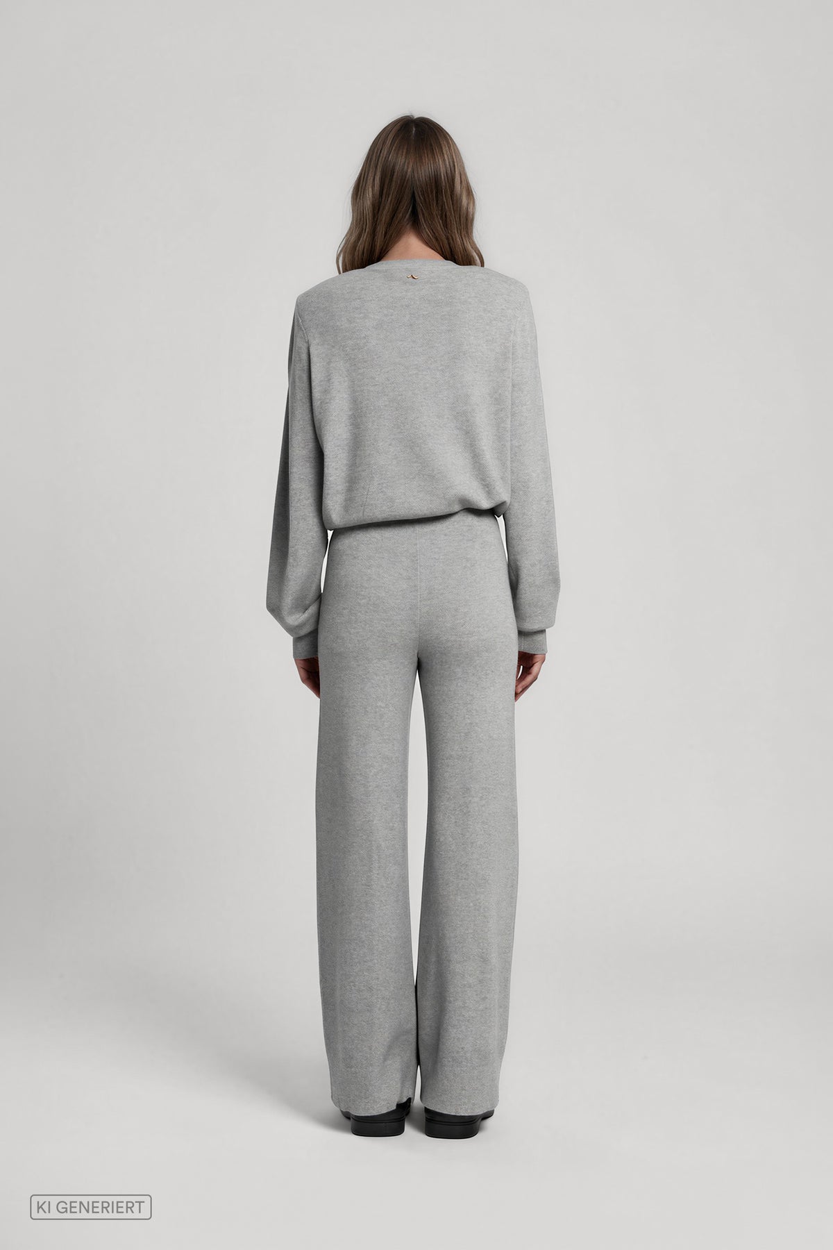 Rückansicht eines Models in einem hellgrau melierten Strickset aus langärmligem Pullover und weit geschnittener Strickhose.