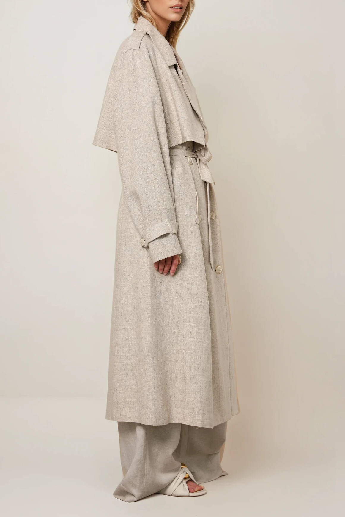 Seitenansicht eines langen Trenchcoats in Beige Melange mit Reverskragen, Bindegürtel und lockerer Passform.