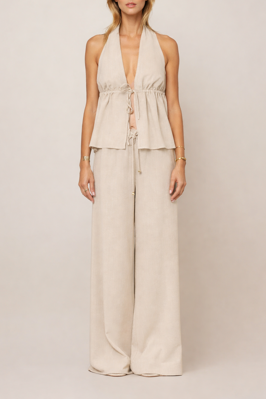 Beigefarbenes Halterneck-Top mit tiefem V-Ausschnitt und Tunnelzug unter der Brust, locker fallend, kombiniert mit weiter Hose im Lookbild.