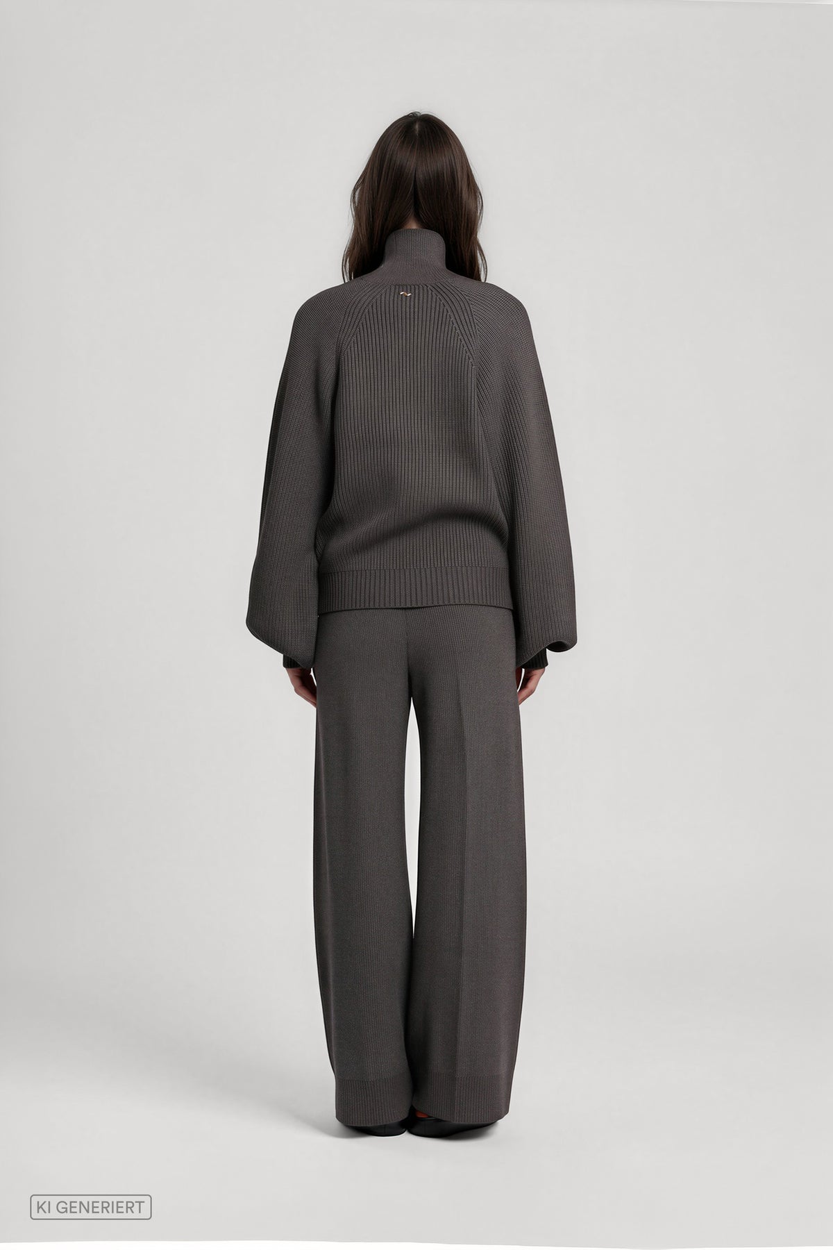 Rückansicht eines Models in einem dunkelgrauen Strickset aus geripptem Pullover mit Rollkragen und weit geschnittener Strickhose.