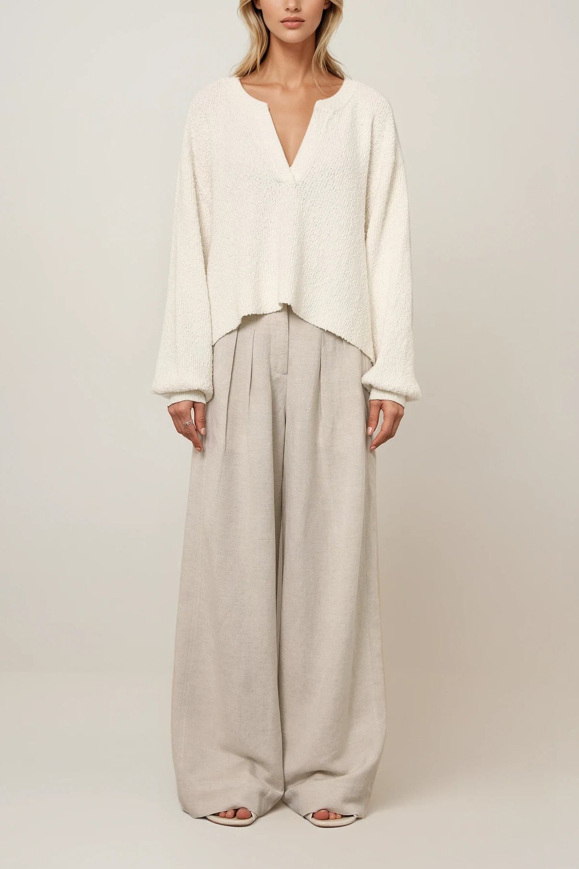 Off-White Strickpullover mit V-Ausschnitt und strukturierter Oberfläche, locker geschnitten mit langen Ärmeln, kombiniert mit weiter, beigefarbener Hose im Lookbild sowie als Einzelansicht vor hellem Hintergrund.