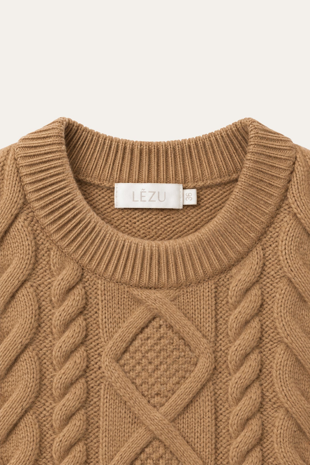 Nahaufnahme eines camelbraunen Strickpullovers mit Rundhalsausschnitt, markantem Zopfmuster und sichtbarem LEZU-Etikett am Kragen.