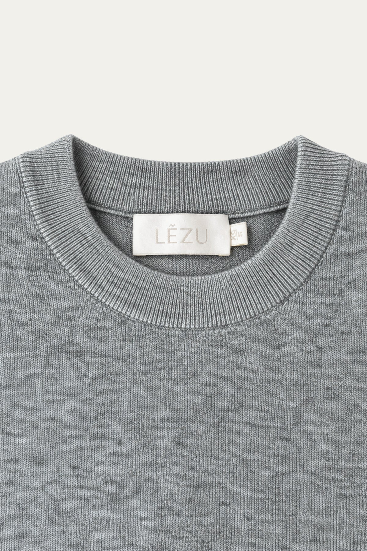 Detailansicht eines hellgrau melierten Strickpullovers mit geripptem Rundhalsausschnitt und LÉZU-Label im Nackenbereich.
