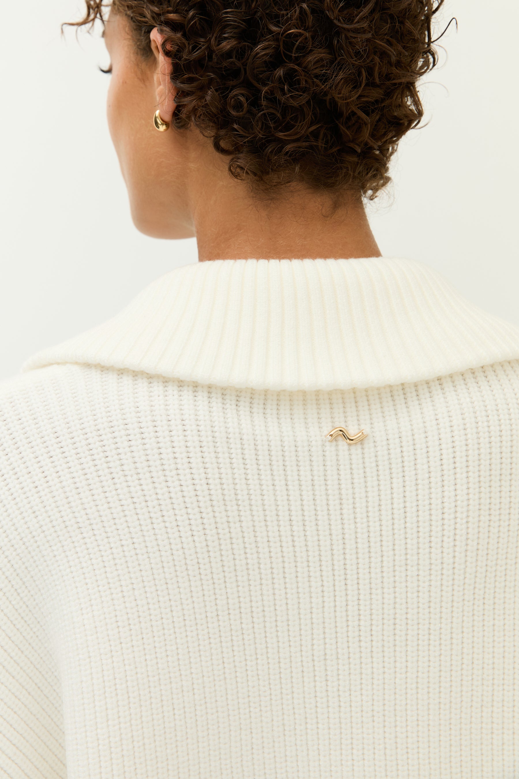    Look 2 – Strickset in Off-White (Bilder 7–12):
Modell trägt ein zweiteiliges Set aus weichem, geripptem Strick in Off-White, bestehend aus einem langärmeligen Zip-Cardigan mit breitem Kragen, goldfarbenem Reißverschluss und zwei großen aufgesetzten Taschen sowie einer weit geschnittenen Hose mit fließendem Fall. Auf der Rückseite der Jacke ist ein kleines, goldfarbenes Lezu-Logo unter dem Kragen platziert. Styling mit beigen Slippern.