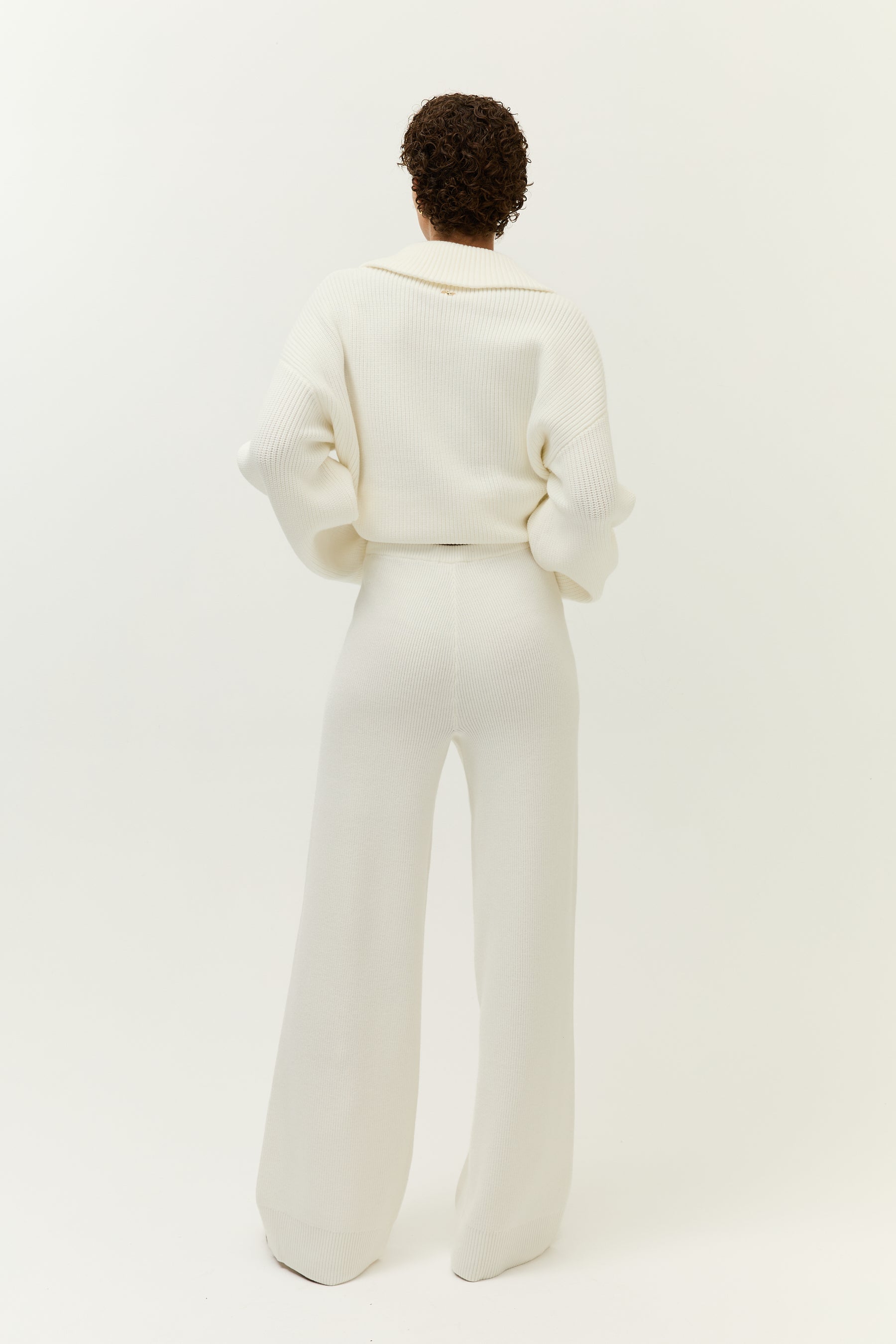 Rückenansicht des weißen Strickensembles mit betonter Taille, lockerem Oberteil und weitem Bein.