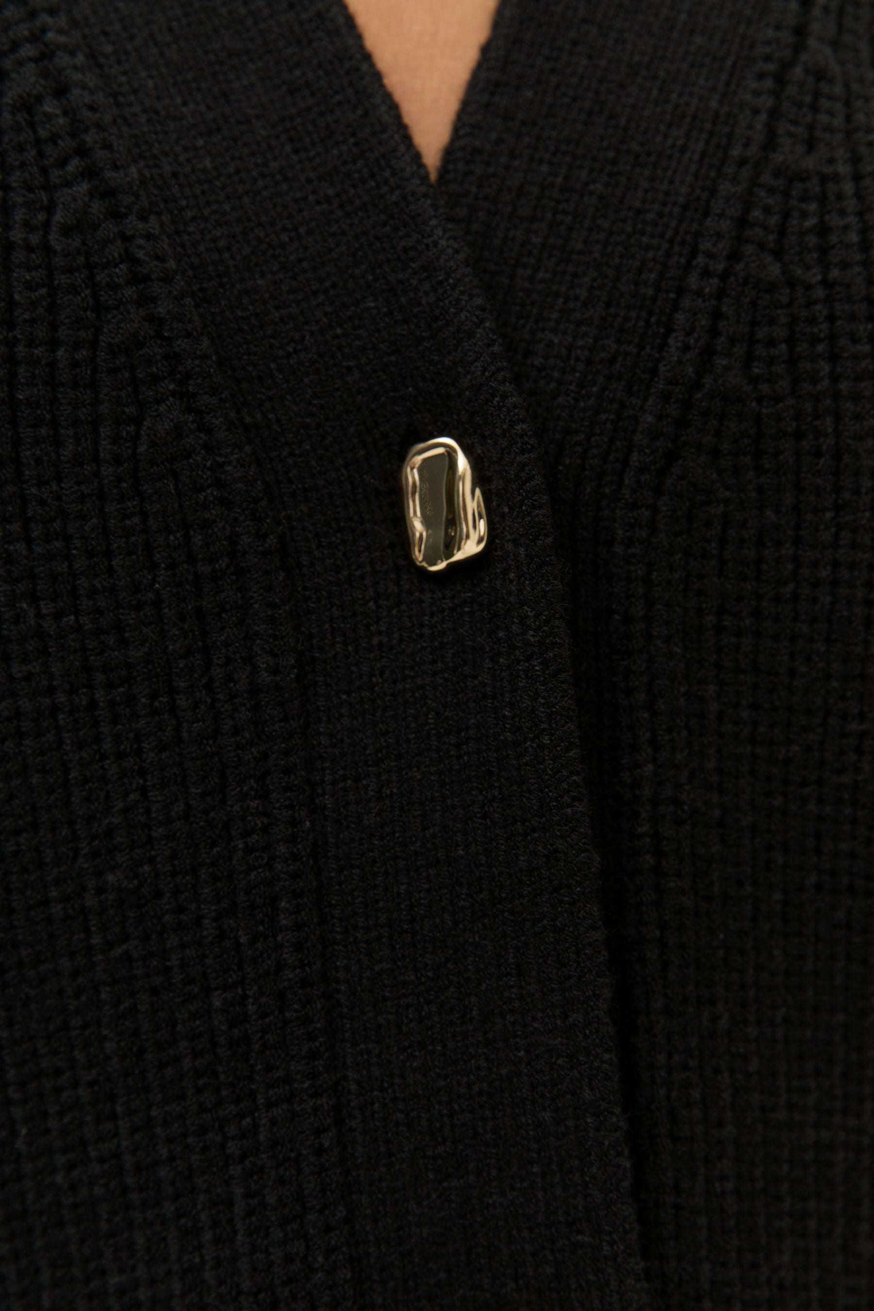 Nahaufnahme eines einzelnen goldenen Knopfes auf dem Strickmaterial des Cardigans.