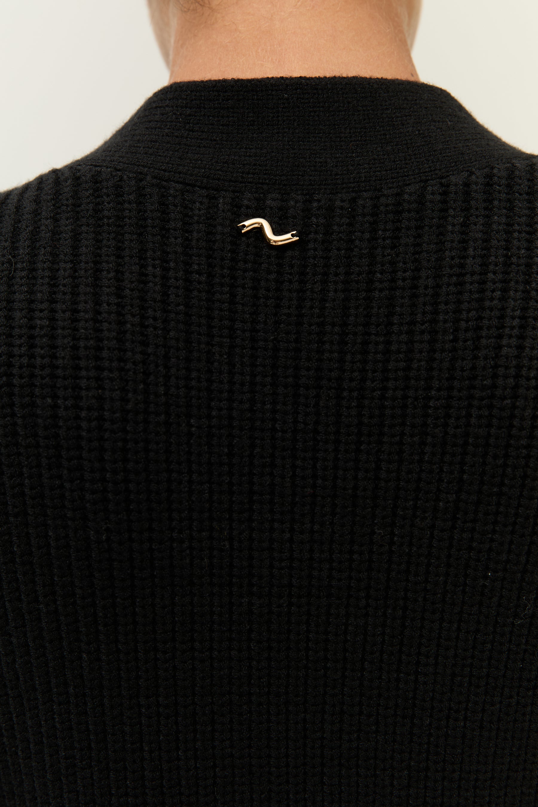 Detailaufnahme des kleinen goldenen Lezu-Logos auf dem oberen Rücken des Cardigans.
