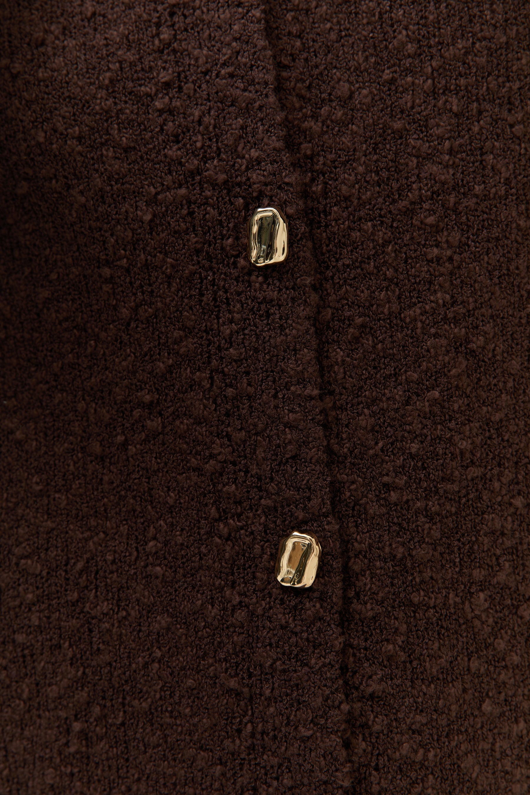 Detailaufnahme Knopfleiste: Die strukturierte Bouclé-Oberfläche und zwei goldene Knöpfe sind im Close-up sichtbar.