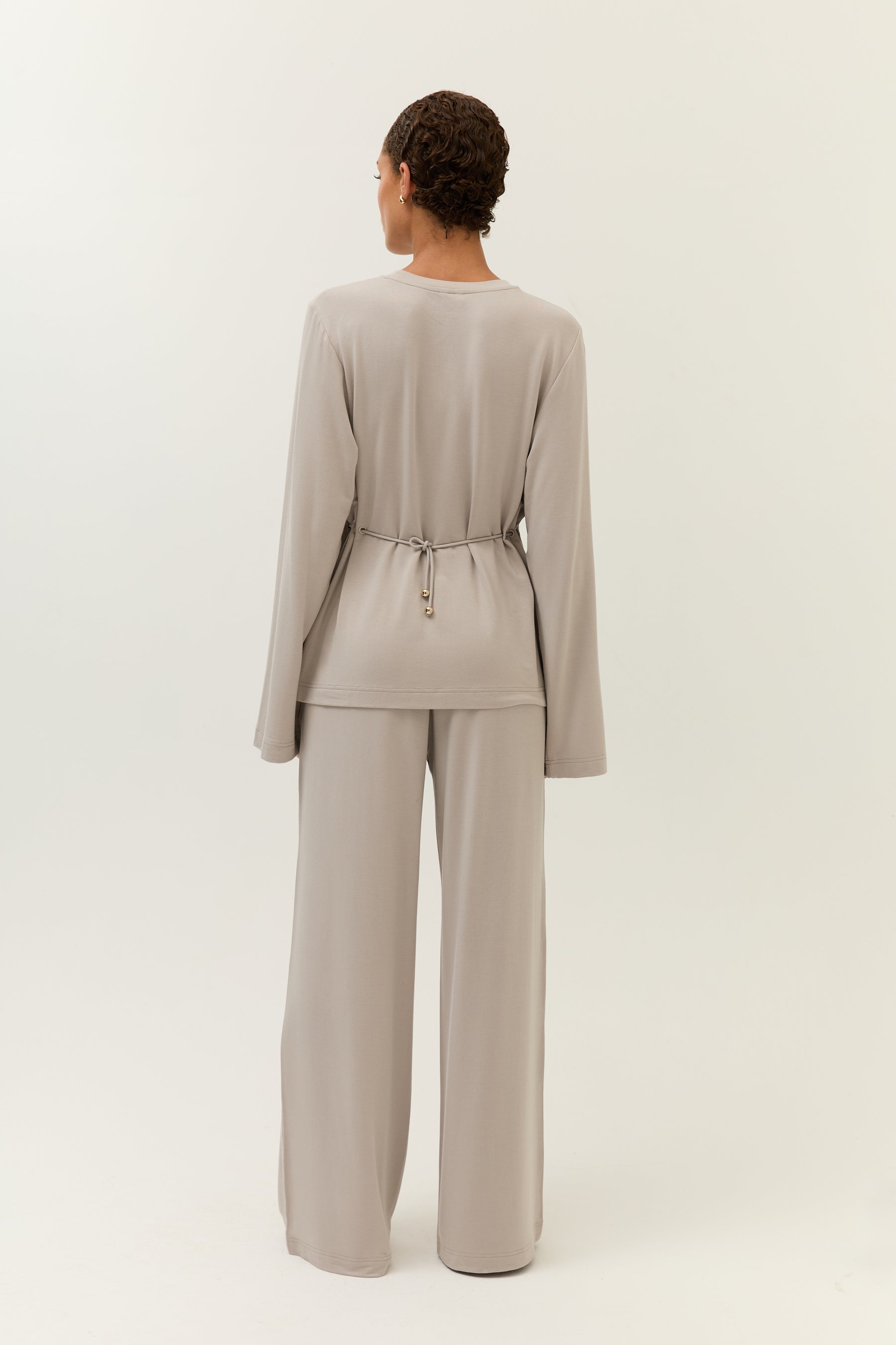 Rückenansicht des Looks
Komplettes Rückansichtsbild des taupefarbenen Sets mit langärmligem Oberteil und locker fallender, weiter Hose.