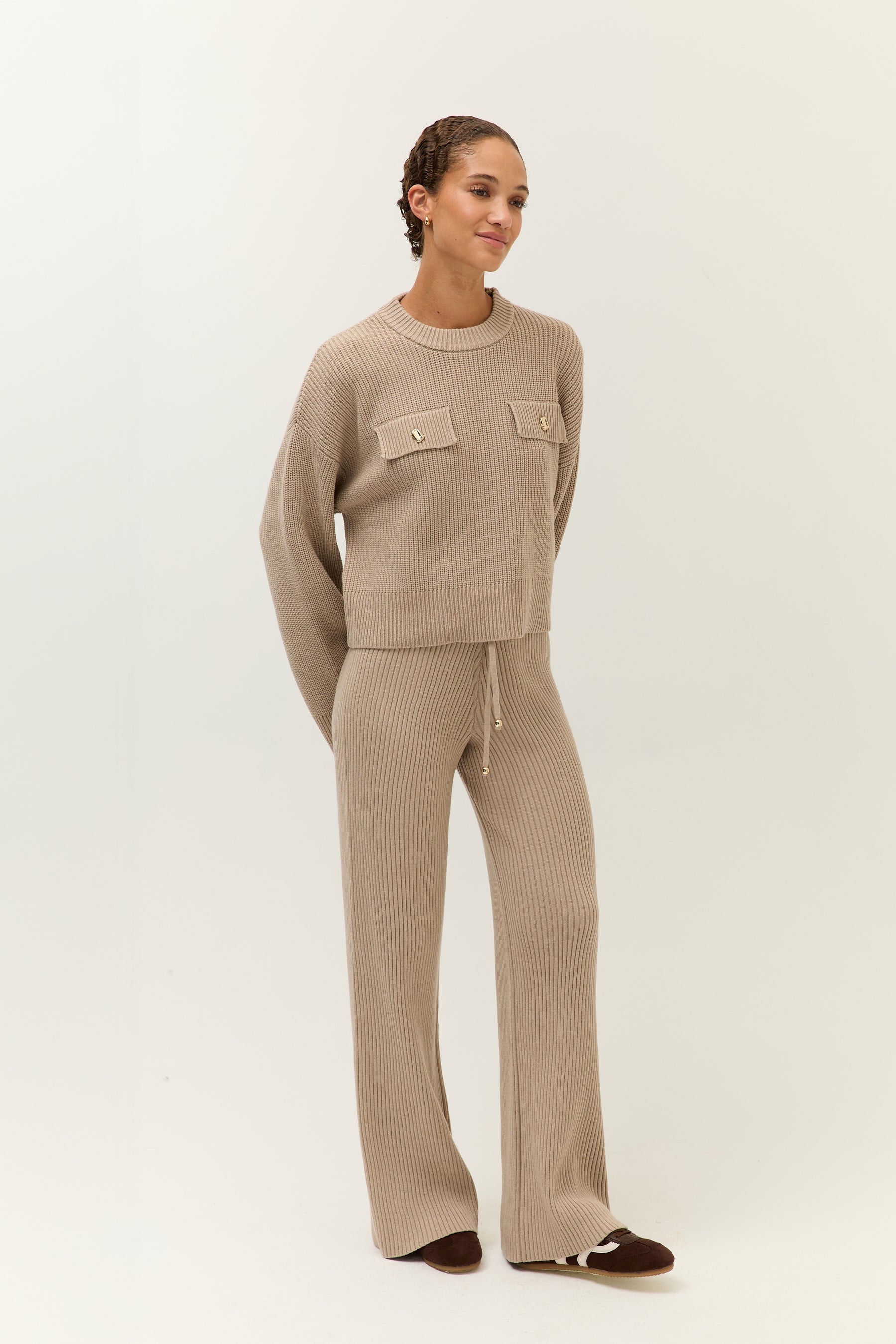 Seitliche Ansicht des beigen Strick-Ensembles mit lockerem Pullover und ausgestellter Hose, kombiniert mit Hausschuhen.