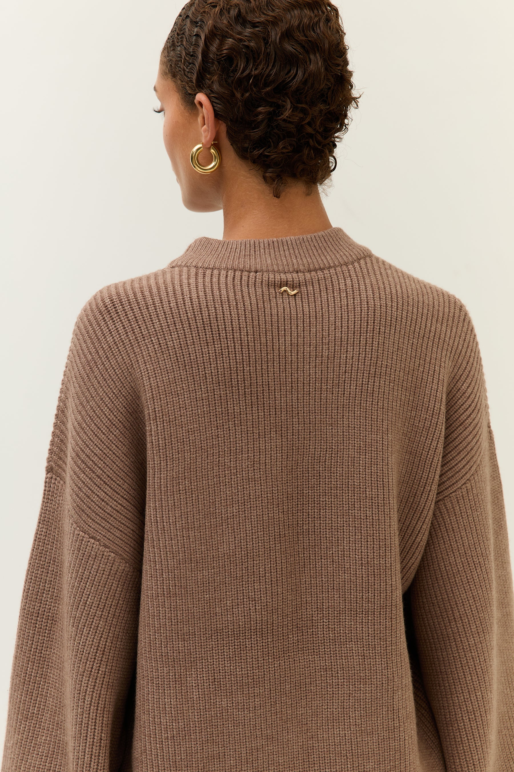 Bild 4: Rückansicht des Pullovers mit Fokus auf das kleine, goldene Lezu-Logo im Nackenbereich. Das Strickmuster ist grob gerippt.