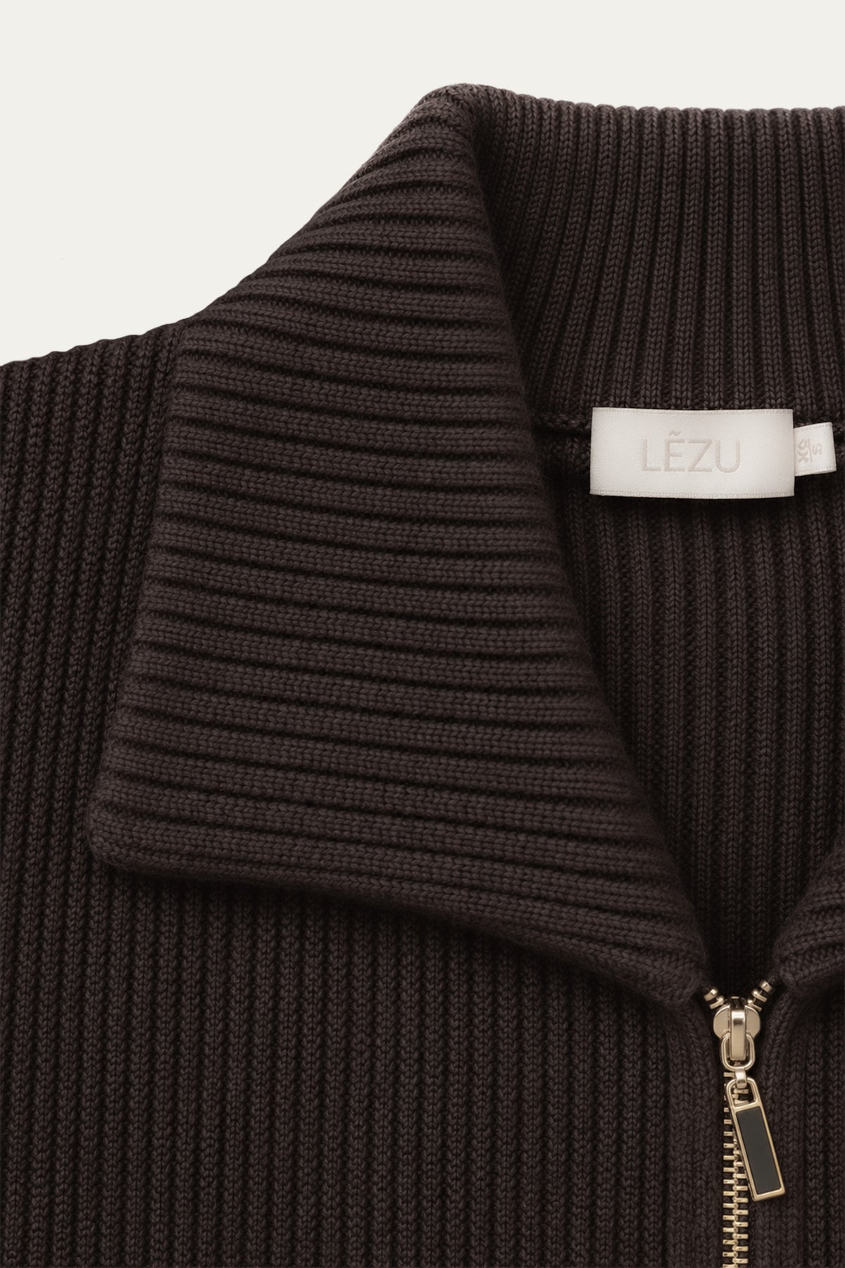 Detailaufnahme eines dunkelbraunen Strickoberteils mit breitem geripptem Kragen, goldenem Reißverschluss und hellem LEZU-Label.