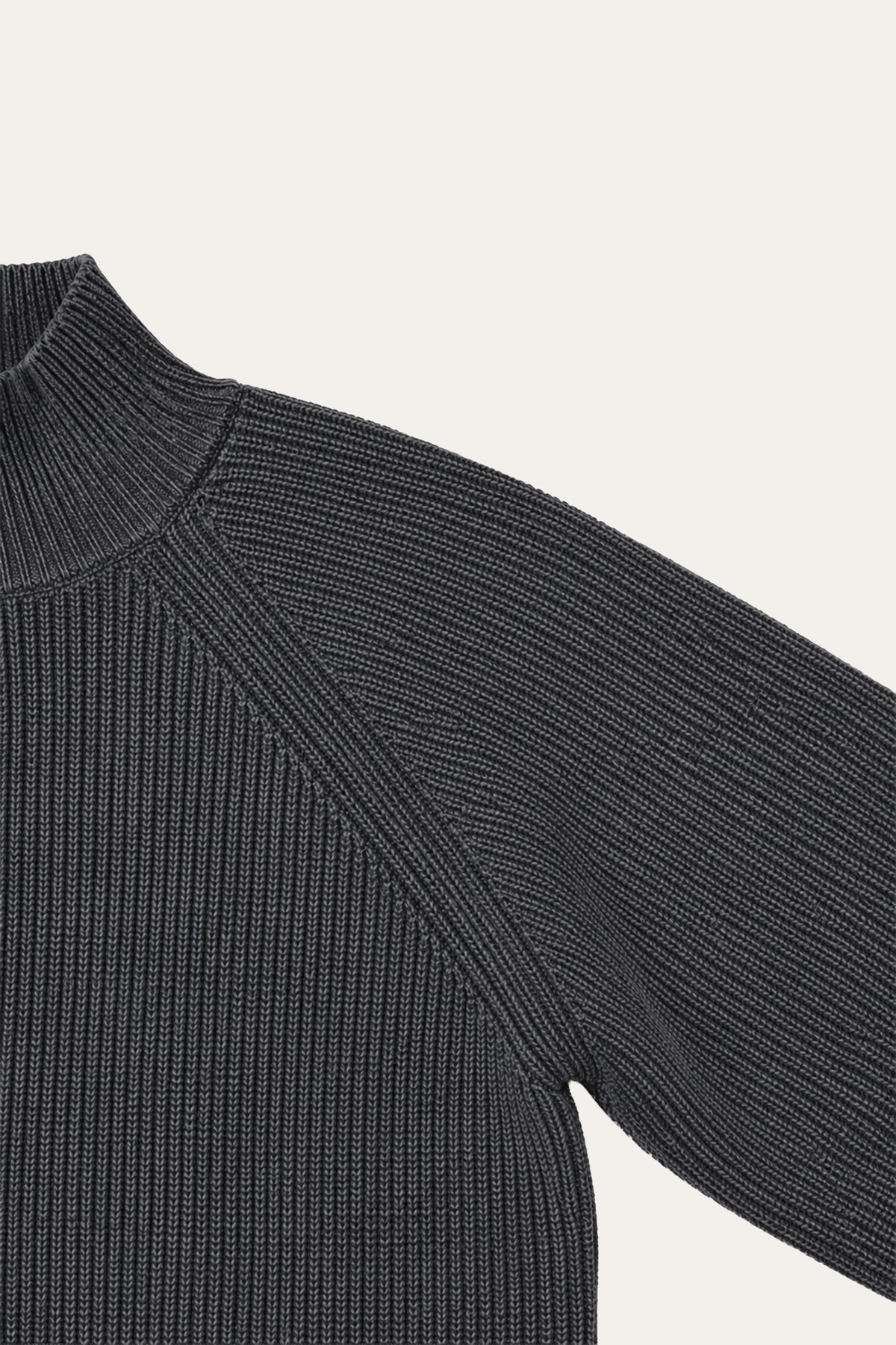 Detailansicht eines schwarzen Rippstrickpullovers mit hohem Stehkragen, Raglannaht und strukturiertem Ärmel.
