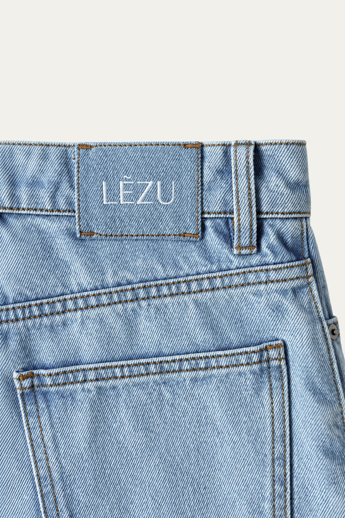Detailansicht der Rückseite einer hellblauen Jeans mit Gesäßtasche, Gürtelschlaufe, kontrastierenden Nähten und LEZU-Logo am Bund.