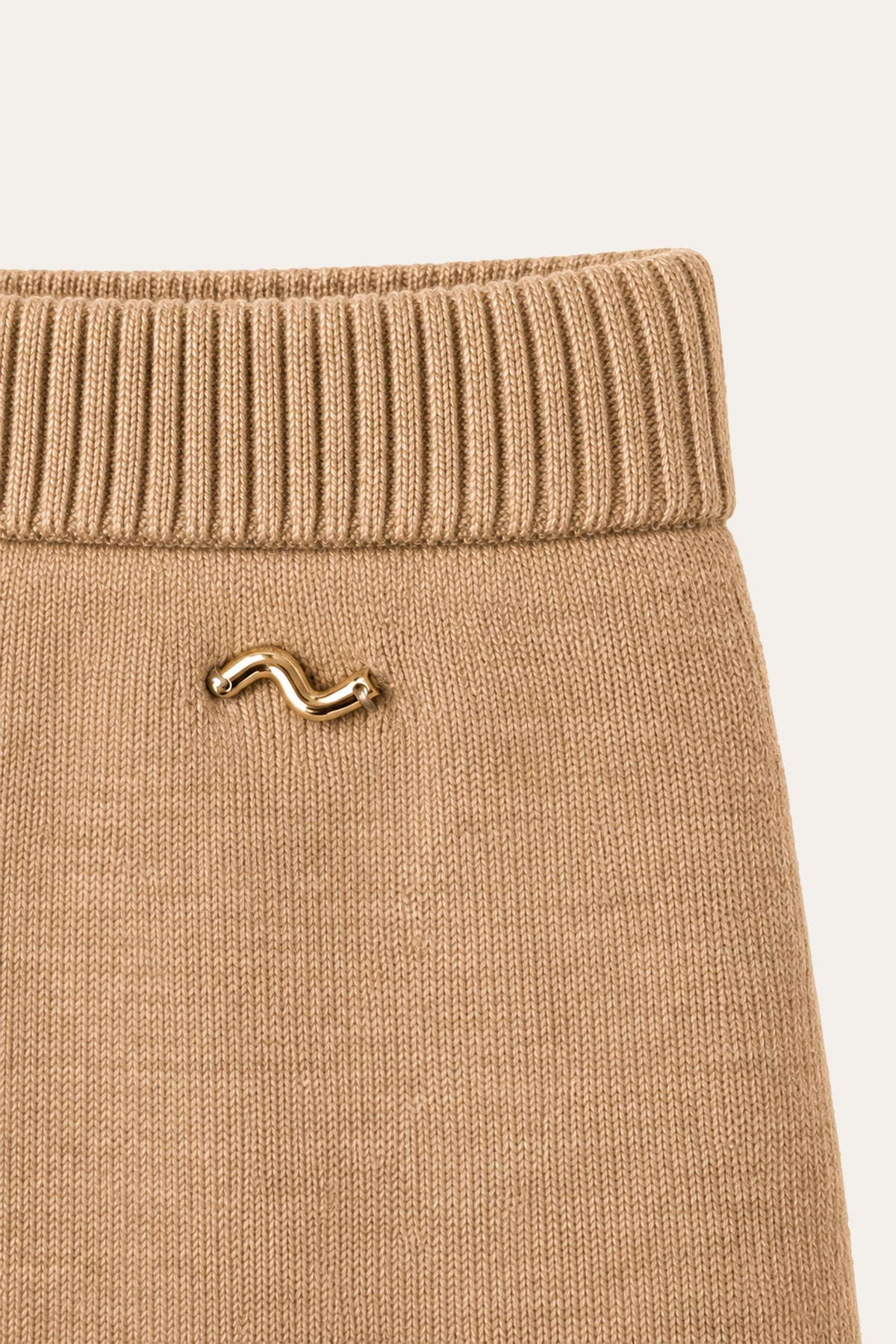 Detailansicht eines camelbraunen Strickrocks mit breitem Rippbund und goldfarbener Zierschließe.